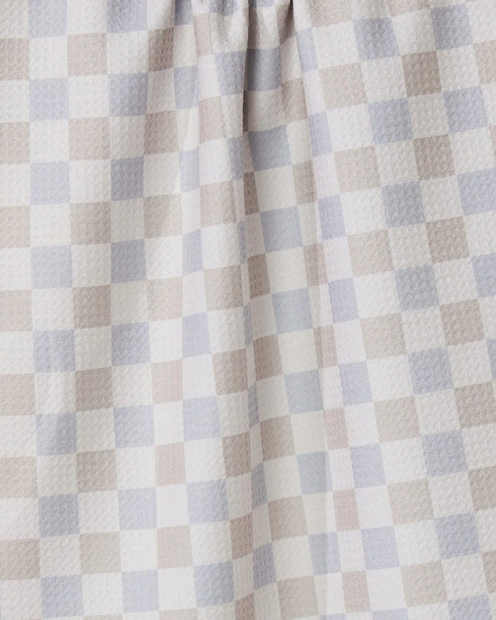 A close-up of the Danse Neutre quick-drying towel by GEOMETRY, featuring a checkered pattern in soft beige, light gray, and white. The fabric is gently gathered at the top, highlighting its texture and folds.