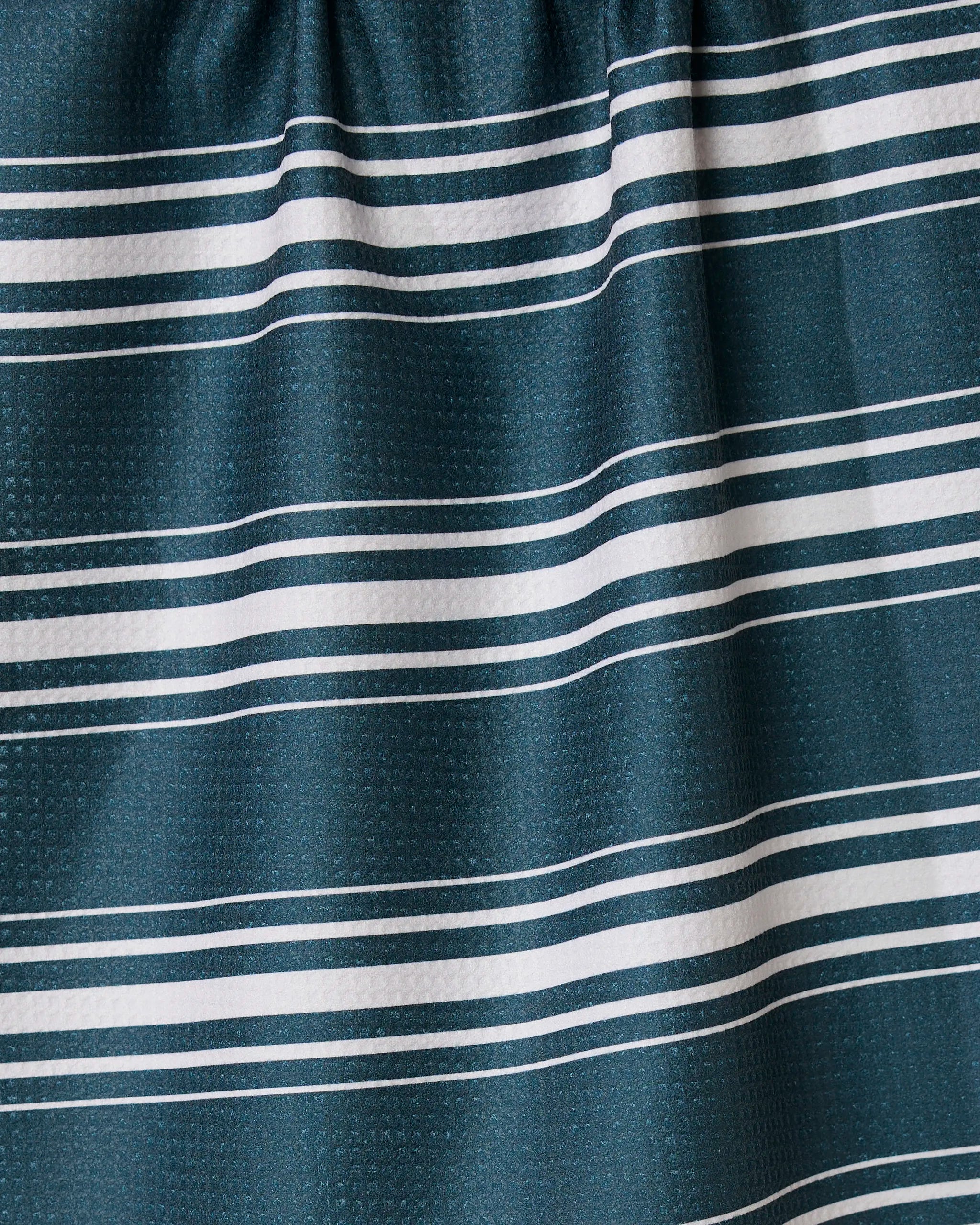 A close-up of GEOMETRYs Deep Blue Fall recycled kitchen towel, showing its textured dark green surface with evenly spaced horizontal white and thin light blue stripes. The fabric is slightly gathered at the top.