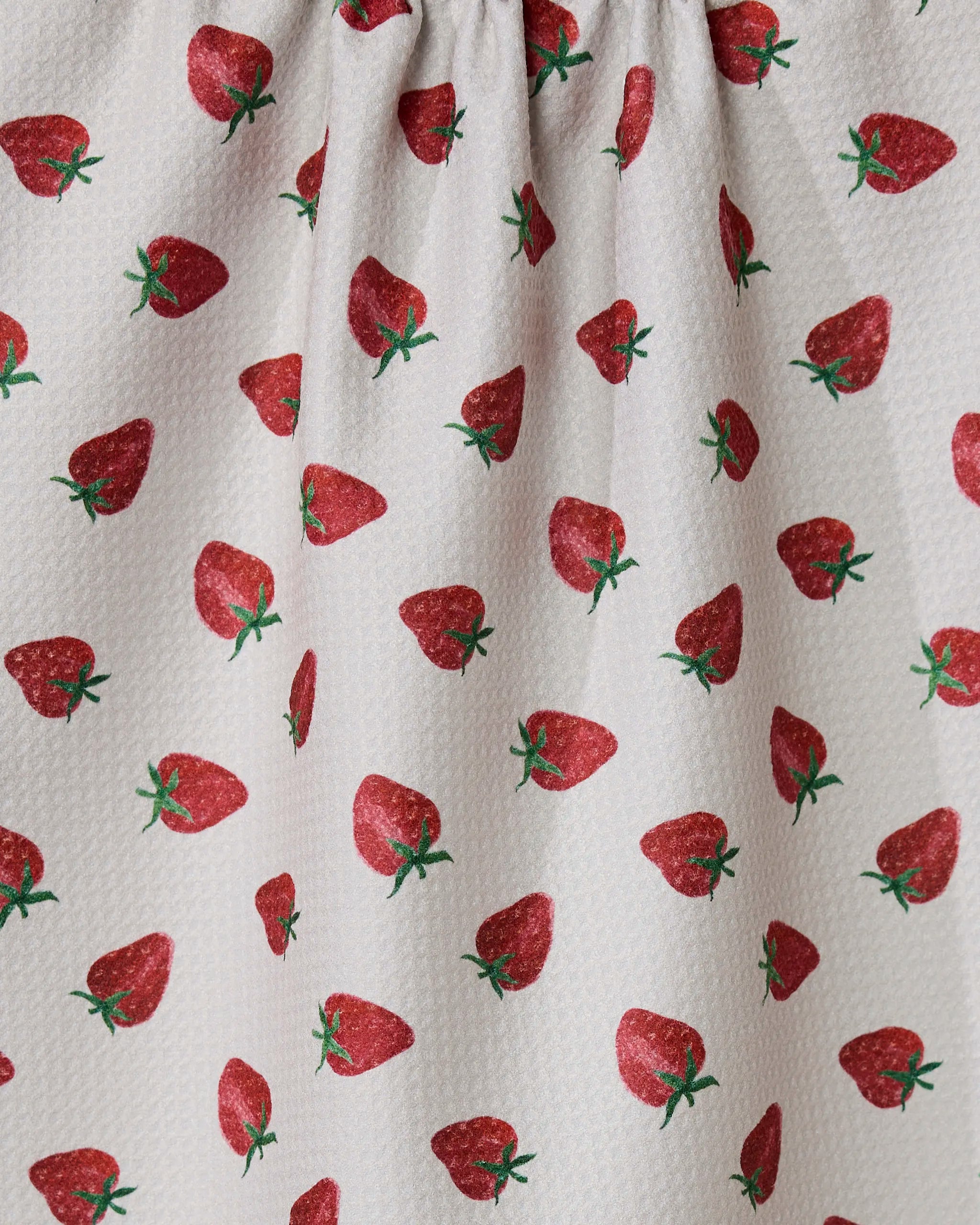 The Berry Patch tea towel by Geometry features a textured white fabric with a repeating red strawberry pattern and green stems. Ultra-absorbent and made from recycled materials, it’s perfect for your kitchen.