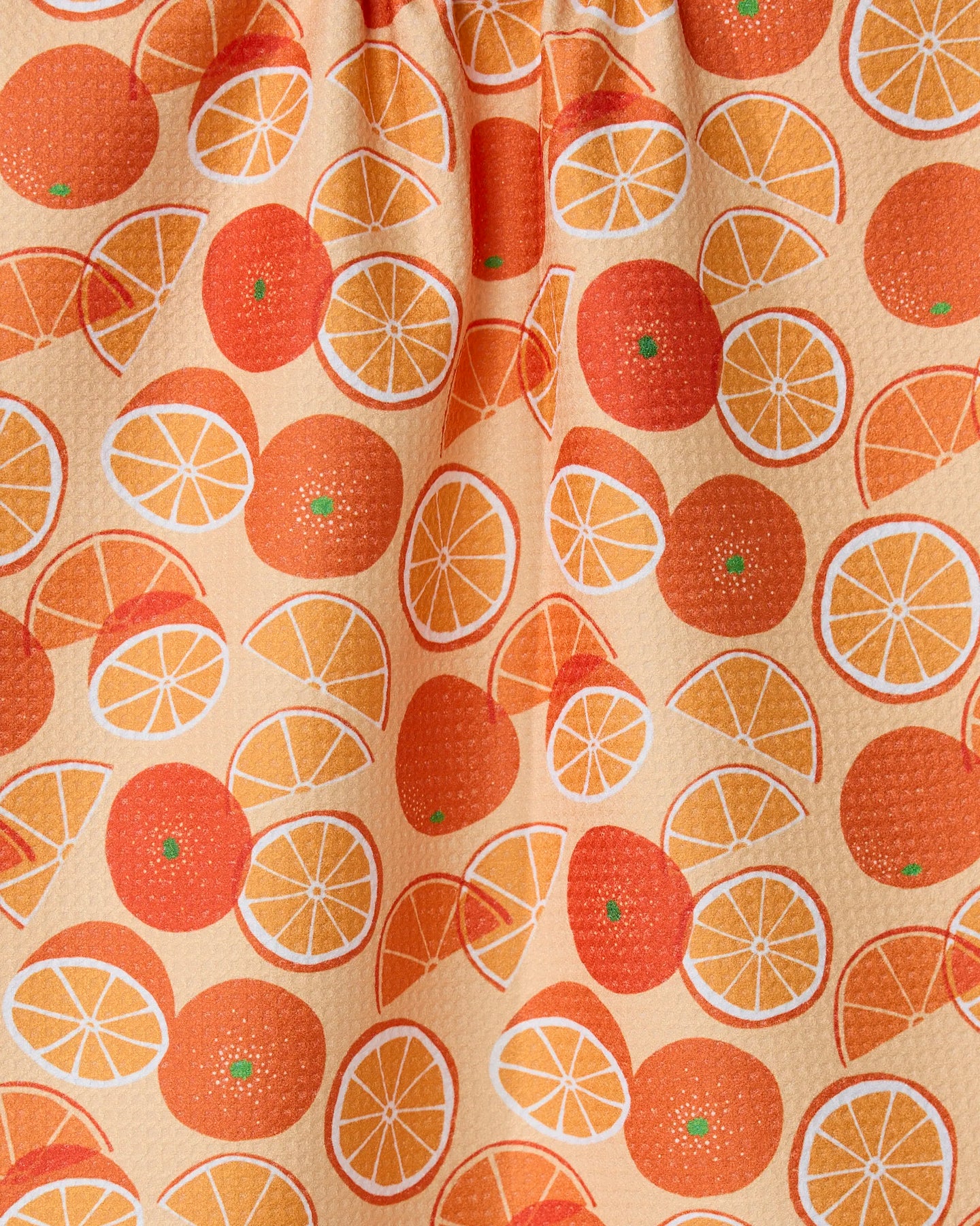 The Geometry Only Oranges tea towel features whole and sliced oranges in orange and yellow hues on a light peach background.