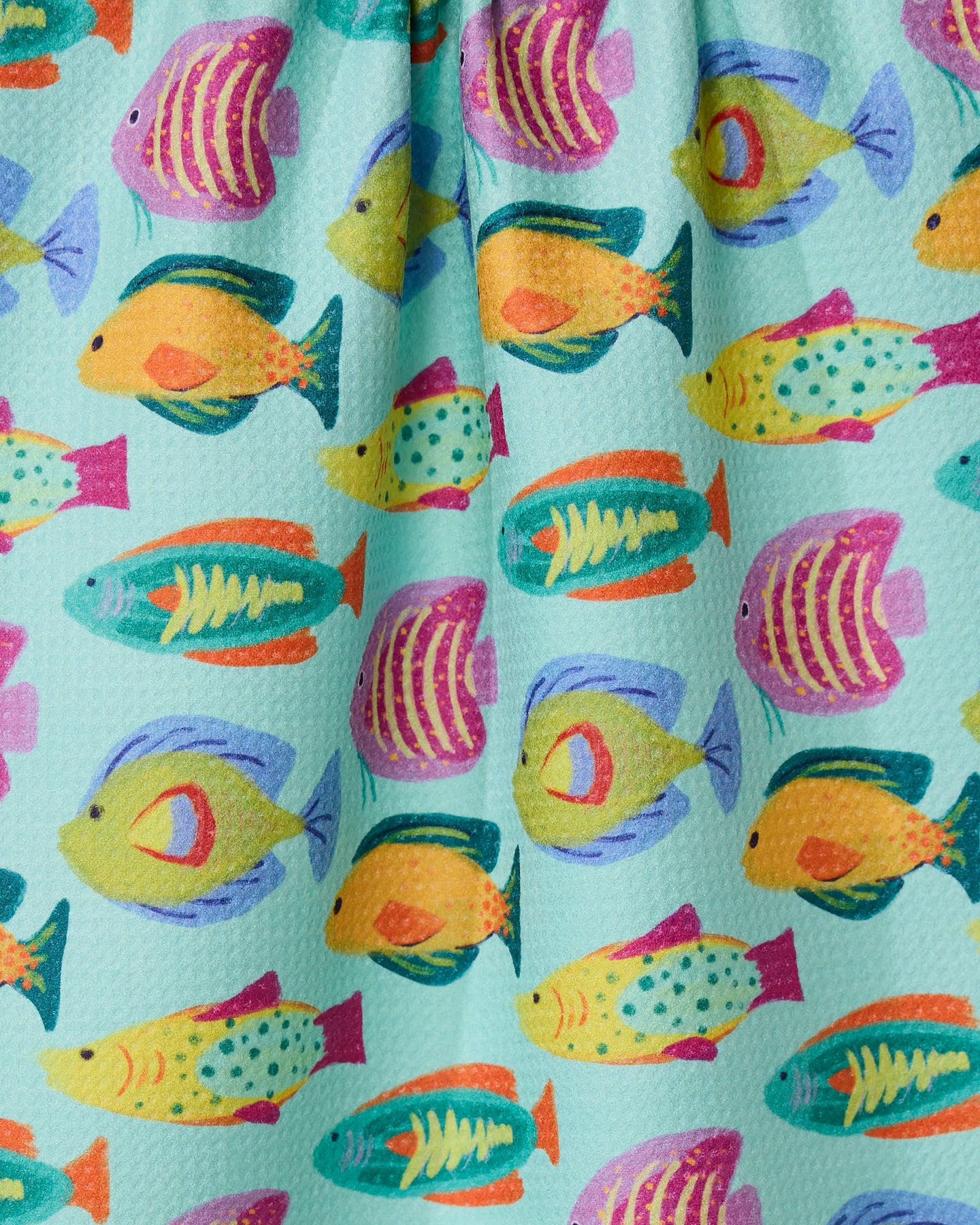 Schooling by Geometry features colorful, cartoon-style fish in yellow, teal, pink, and orange swimming across a light blue textured kitchen towel made from recycled materials.