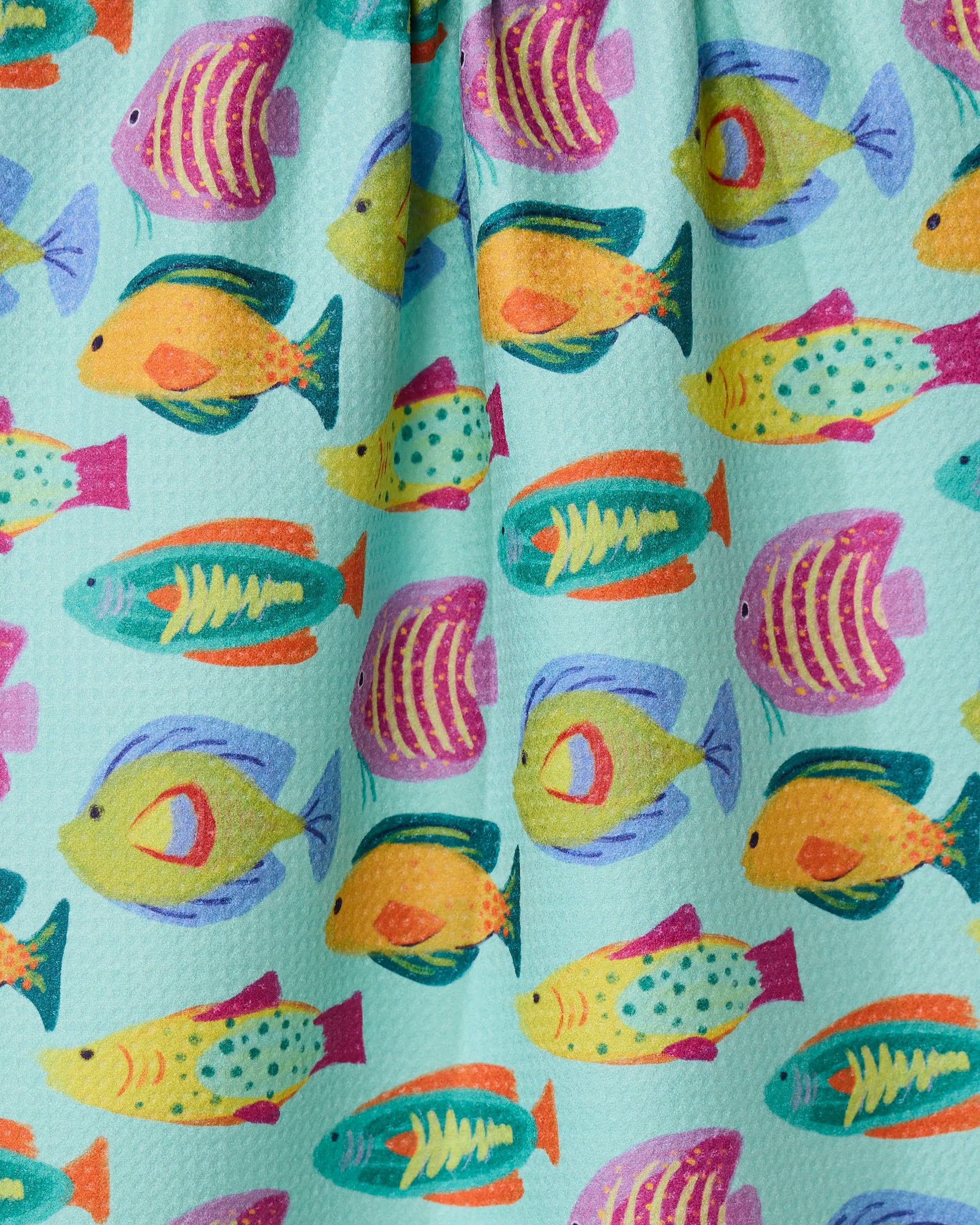 Schooling by Geometry features colorful, cartoon-style fish in yellow, teal, pink, and orange swimming across a light blue textured kitchen towel made from recycled materials.