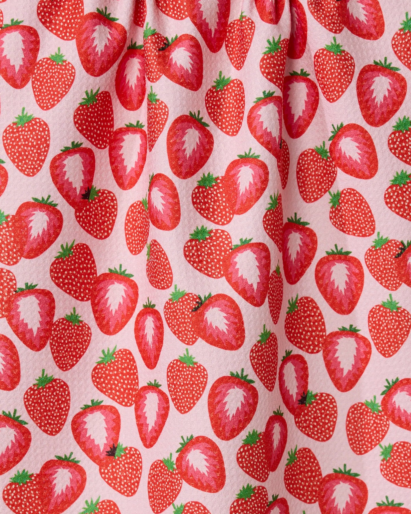 So Many Strawberries by Geometry features a close-up of pink fabric with a lively pattern of whole and sliced red strawberries and green leaves—fun, vibrant, and perfect for a tea towel.