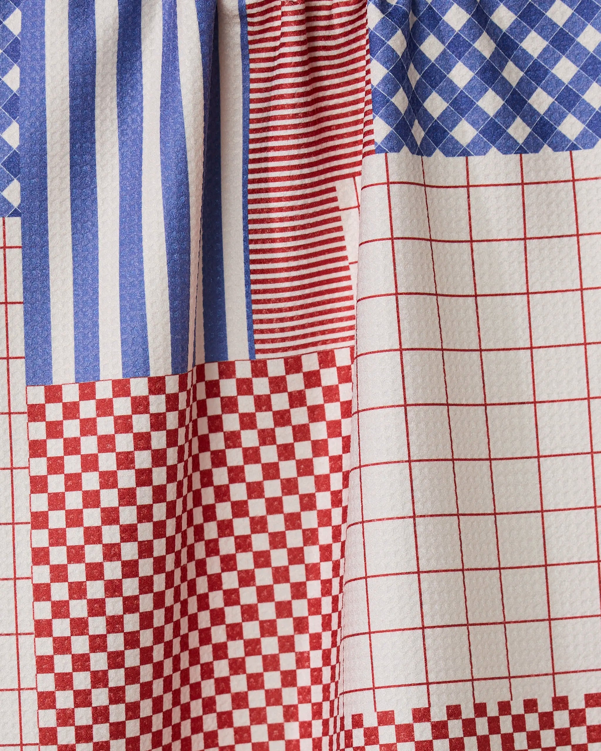A close-up of Geometrys Patched Up Parade, showcasing recycled kitchen towel material in a patchwork of red and blue geometric patterns—stripes, checks, and grids.