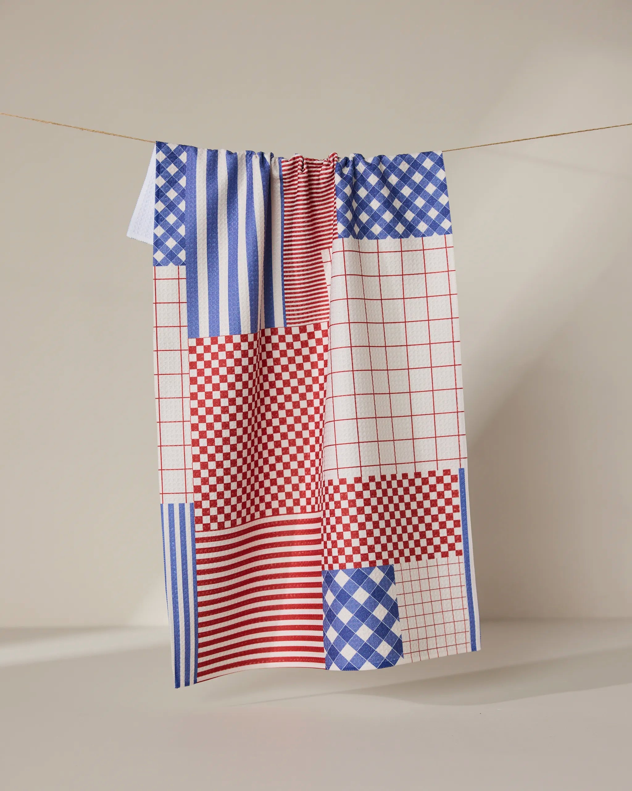 The Geometry Patched Up Parade ultra-absorbent dish towel hangs neatly on a rope.