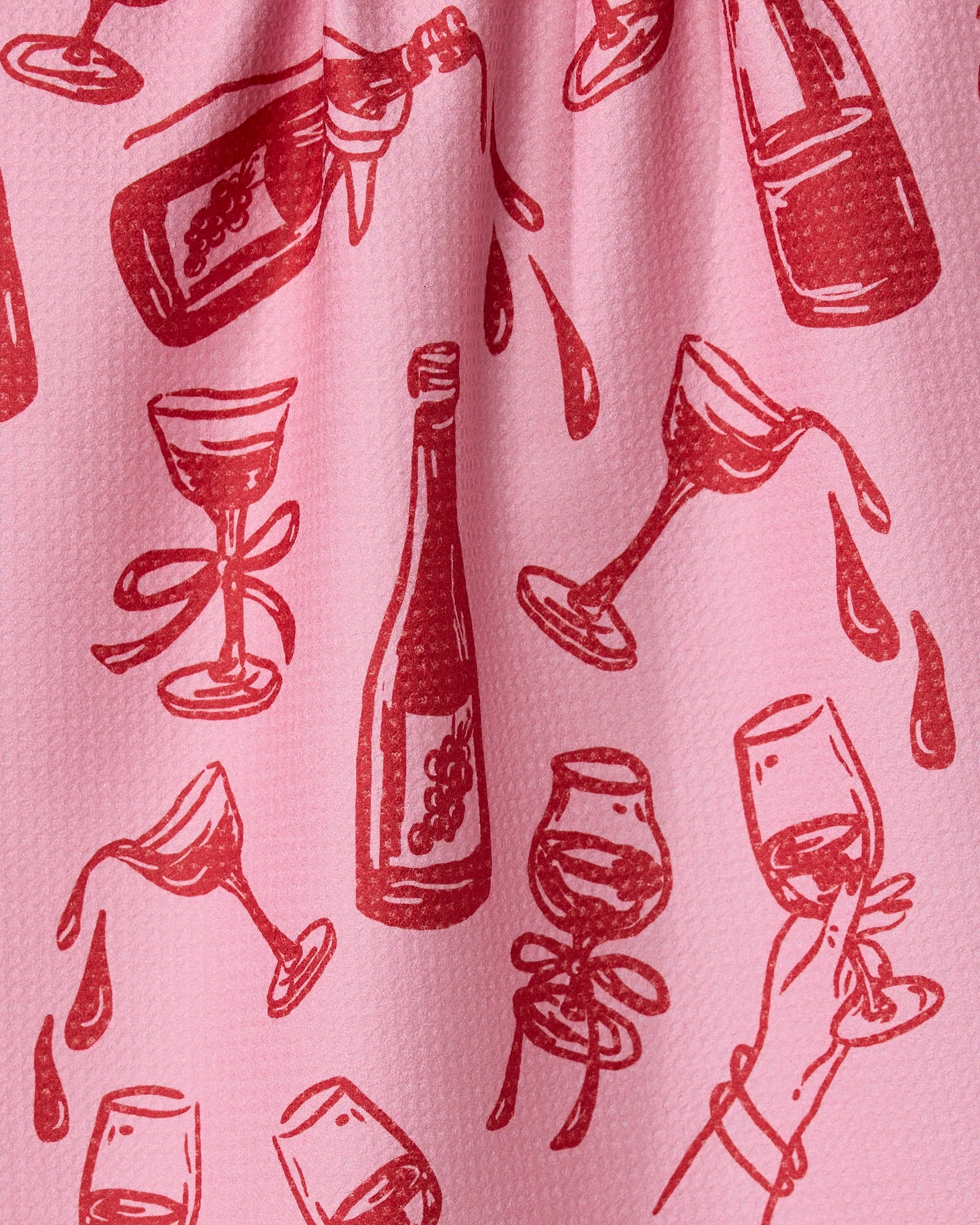 The Geometry Wining and Dining tea towel features a red wine-themed illustrated pattern on pink fabric—bottles, glasses, and more—for a stylish, quick-drying addition to your kitchen.