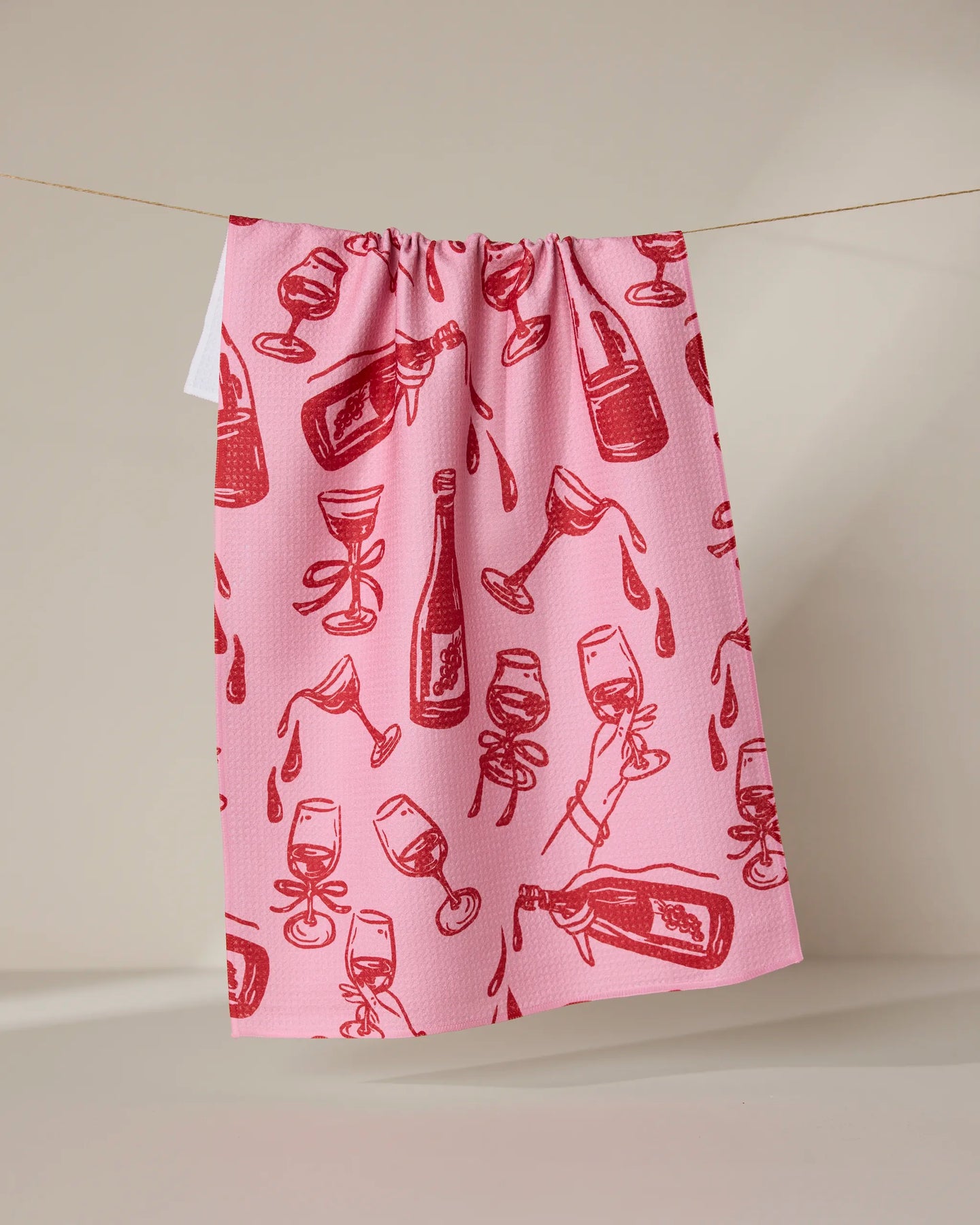 The Geometry Wining and Dining tea towel, in pink, dries quickly and hangs on a line with a red wine bottle and glass pattern featuring playful splashes and spills.