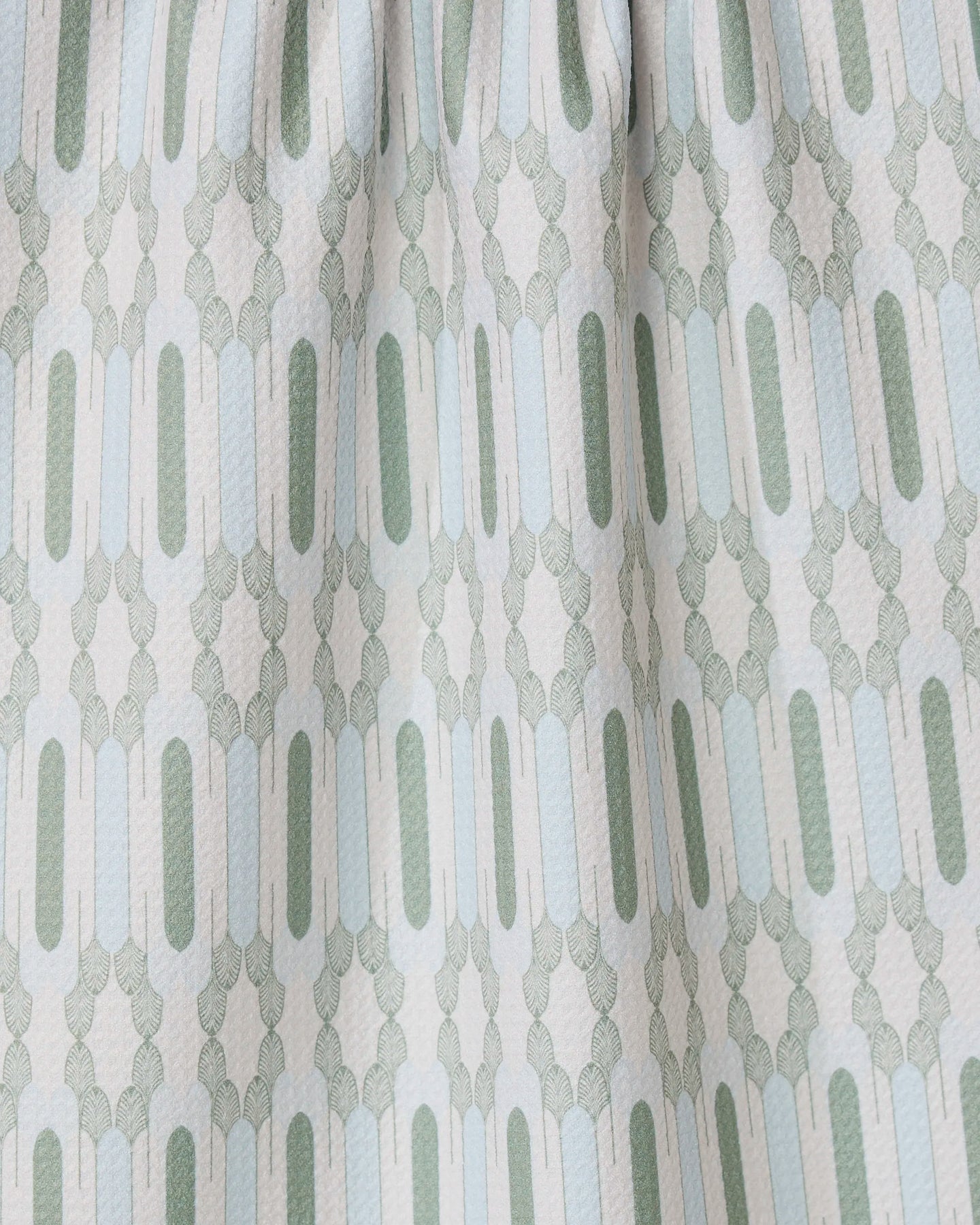 Close-up of the Musée Verte tea towel by GEOMETRY, showcasing a repeating geometric pattern in light green and gray. Made from recycled materials, it features elongated ovals and small shapes with gently gathered fabric at the top.