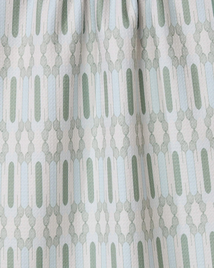 Close-up of the Musée Verte tea towel by GEOMETRY, showcasing a repeating geometric pattern in light green and gray. Made from recycled materials, it features elongated ovals and small shapes with gently gathered fabric at the top.
