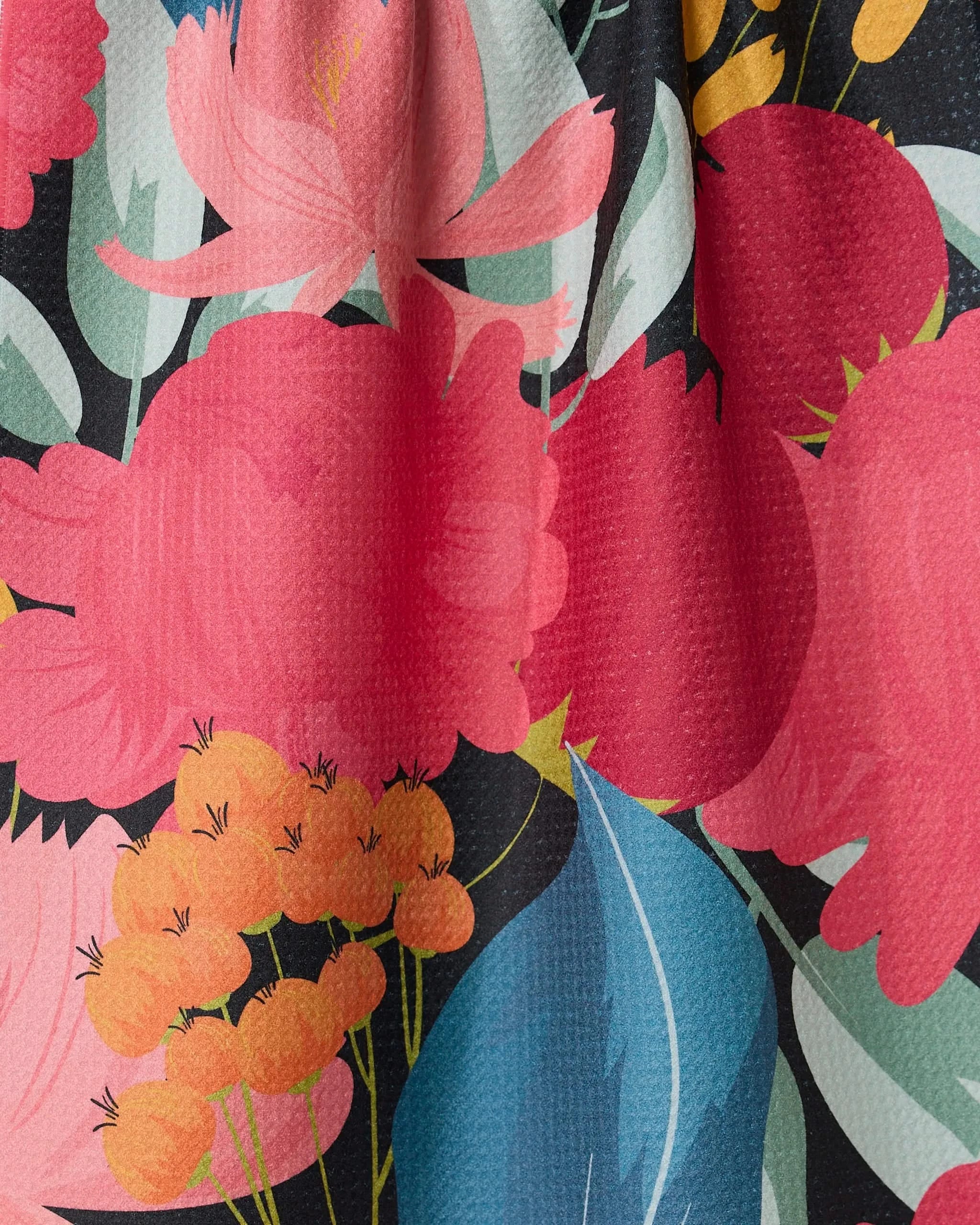 Close-up of GEOMETRYs My Garden tea towel, featuring a colorful floral pattern with bold red and pink flowers, yellow-orange clusters, and teal leaves on black. Super-absorbent Geoweave texture is visible.