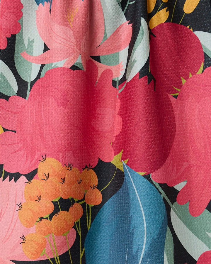 Close-up of GEOMETRYs My Garden tea towel, featuring a colorful floral pattern with bold red and pink flowers, yellow-orange clusters, and teal leaves on black. Super-absorbent Geoweave texture is visible.