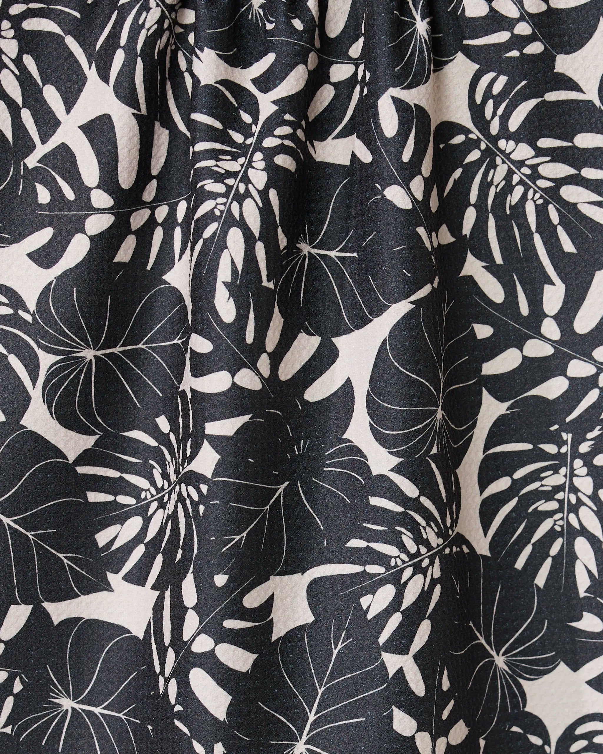 Close-up of GEOMETRYs Neutral Leaves tea towel, made from ultra-absorbent fabric with a black and white stylized monstera leaf pattern on a light background. Fabric is slightly gathered at the top.