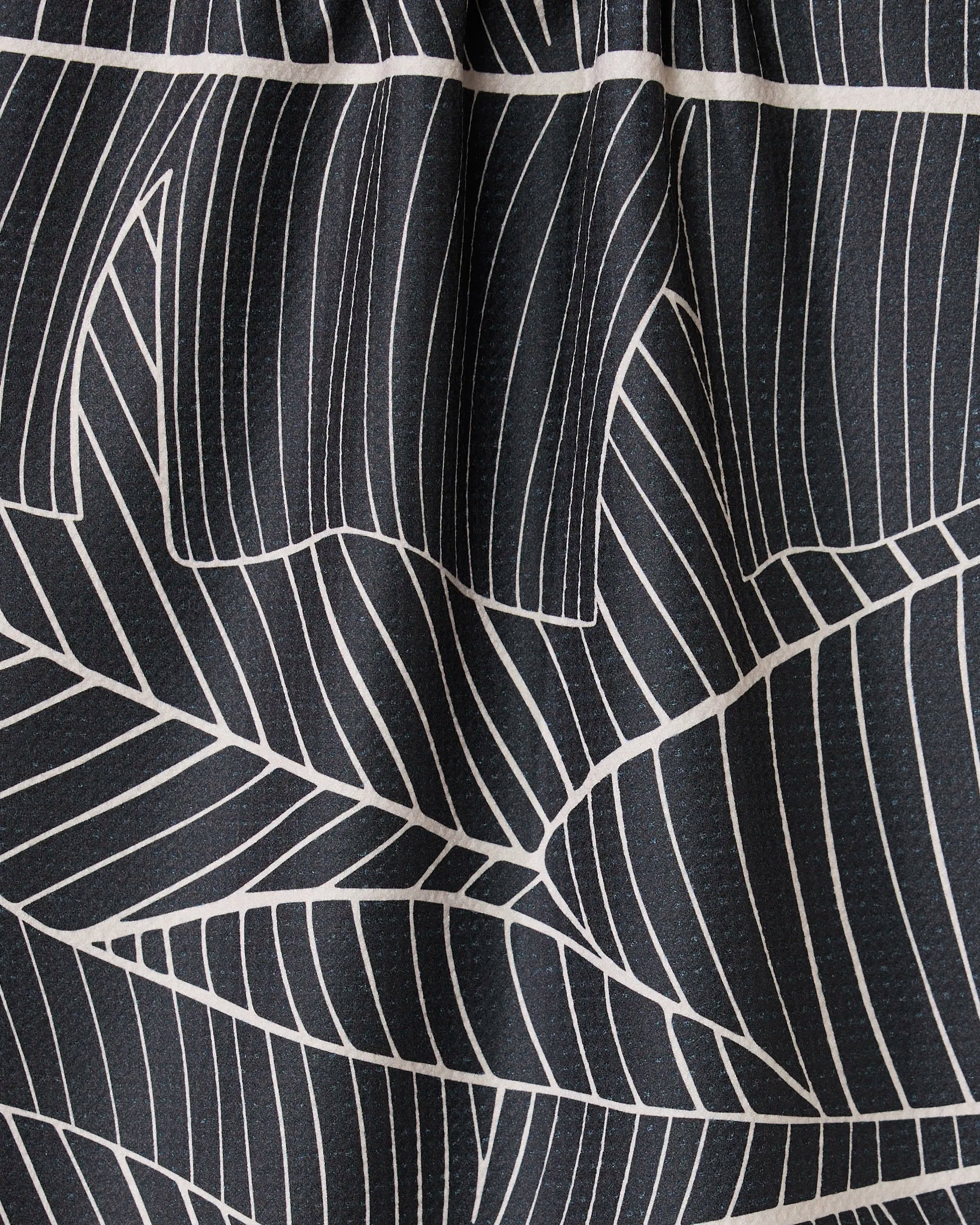 Close-up of GEOMETRYs Neutral Palms: black fabric with bold white geometric palm patterns. The gathered top forms soft pleats and shadows, creating an elegant, modern look.