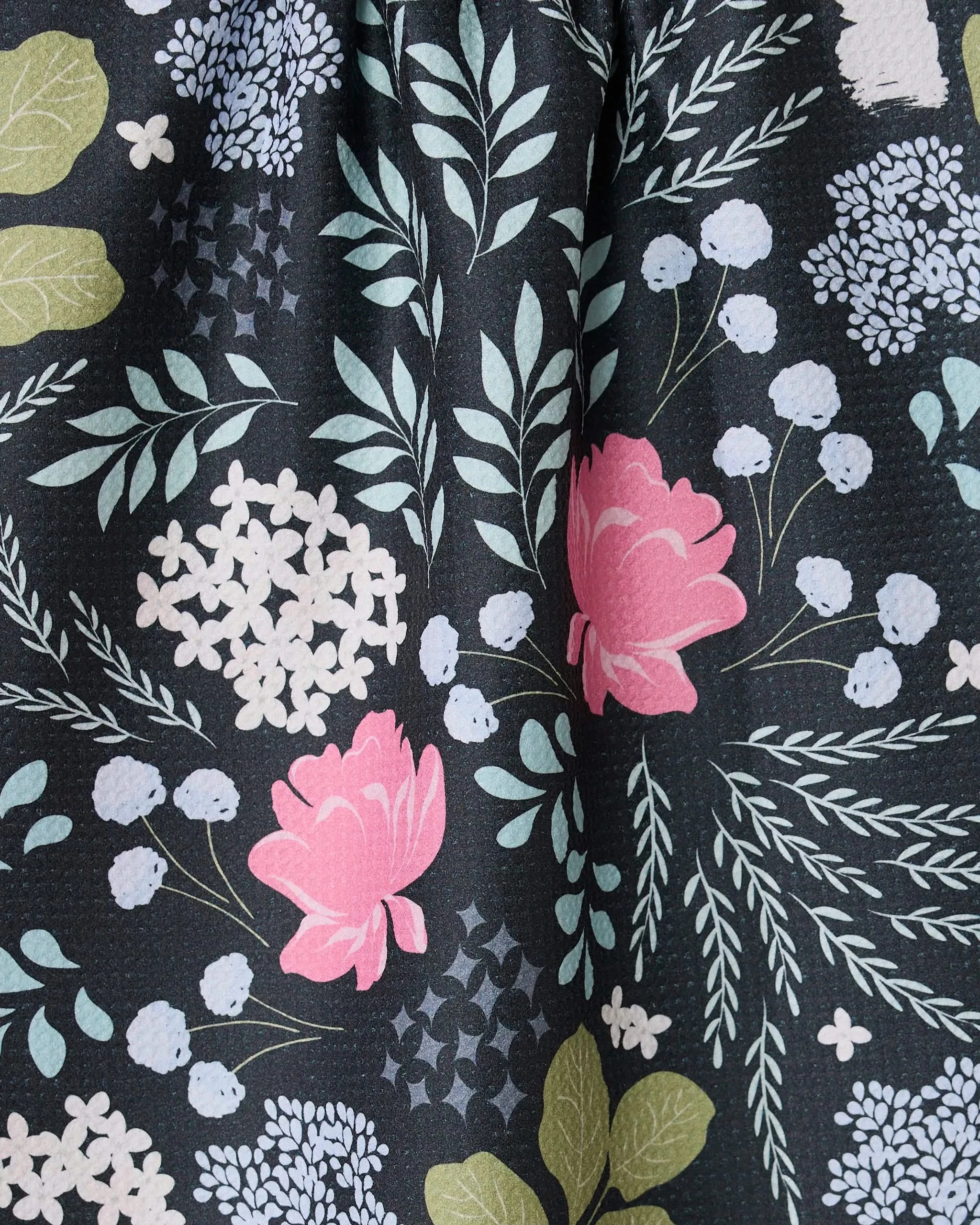 The Not Forgotten towel by GEOMETRY features a whimsical floral pattern with pink roses, white and light blue blooms, and green leaves on black—an ultra-absorbent kitchen essential that adds botanical charm.