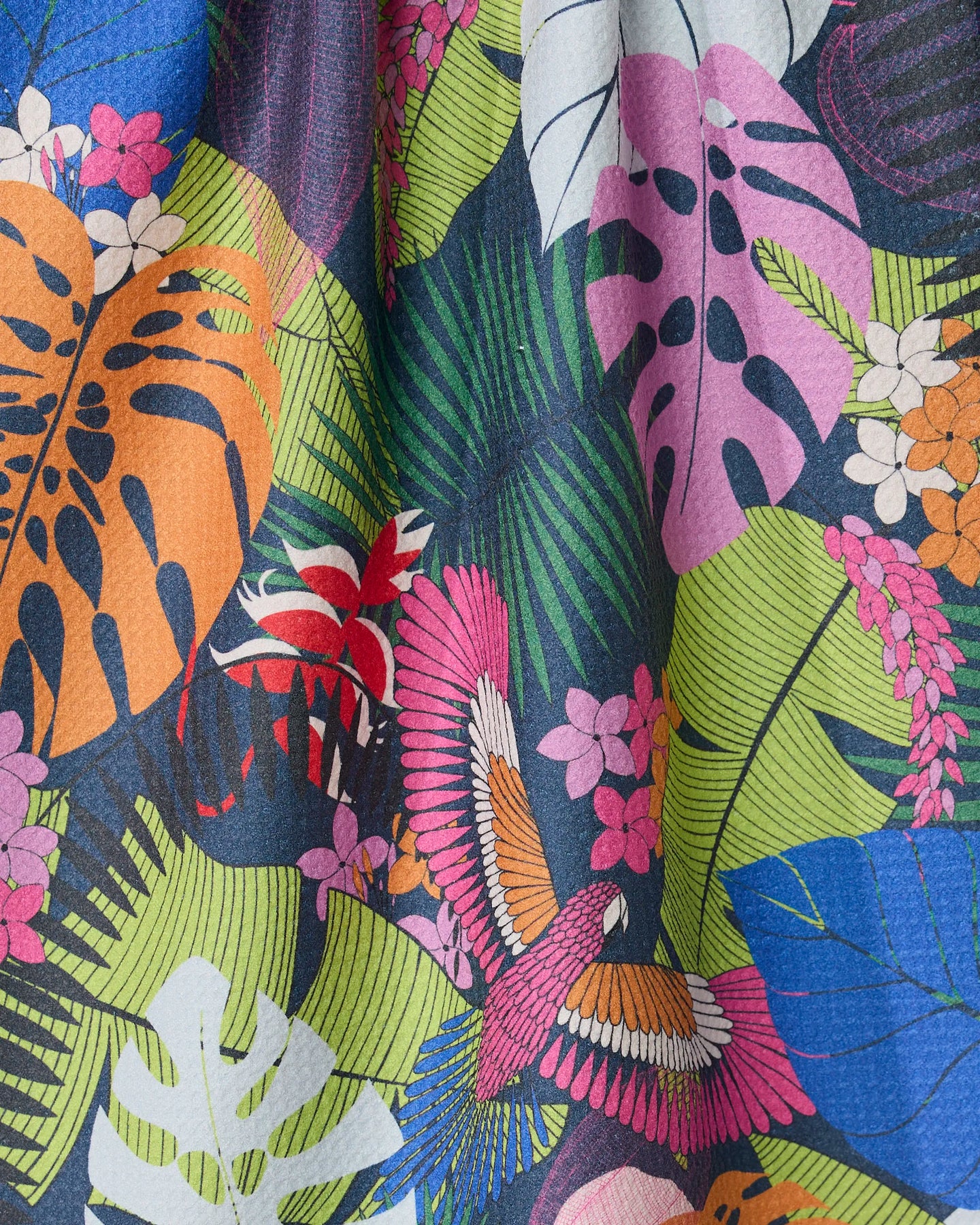 The GEOMETRY Palm Party kitchen towel features colorful recycled fabric with tropical leaves in orange, pink, blue, green, and white, plus a vibrant bird and small pink and orange flowers among the foliage.
