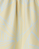 Close-up of the Paradise Blooms tea towel by GEOMETRY, featuring a textured light yellow fabric with a subtle blue abstract leaf pattern and soft folds near the top.