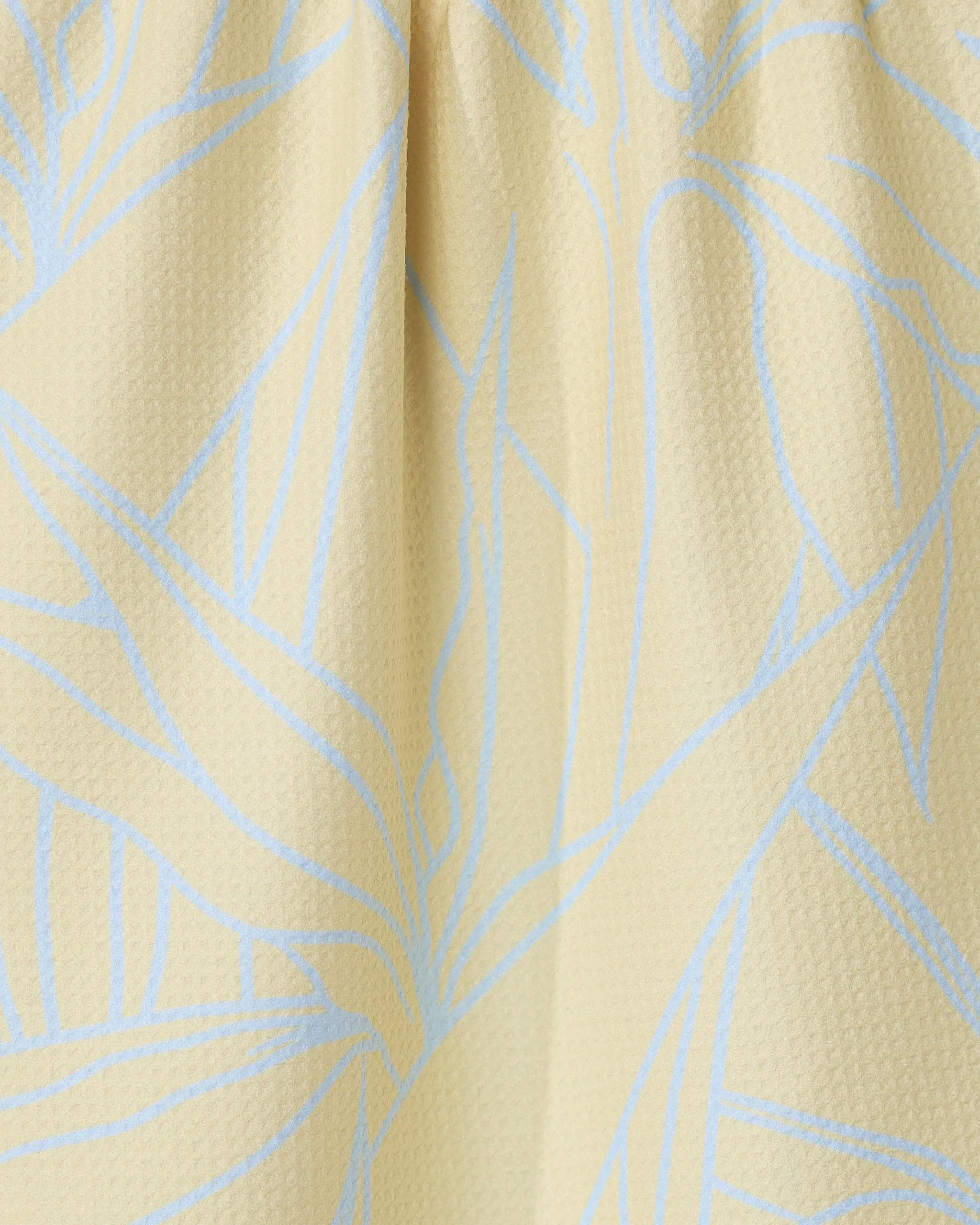 Close-up of the Paradise Blooms tea towel by GEOMETRY, featuring a textured light yellow fabric with a subtle blue abstract leaf pattern and soft folds near the top.
