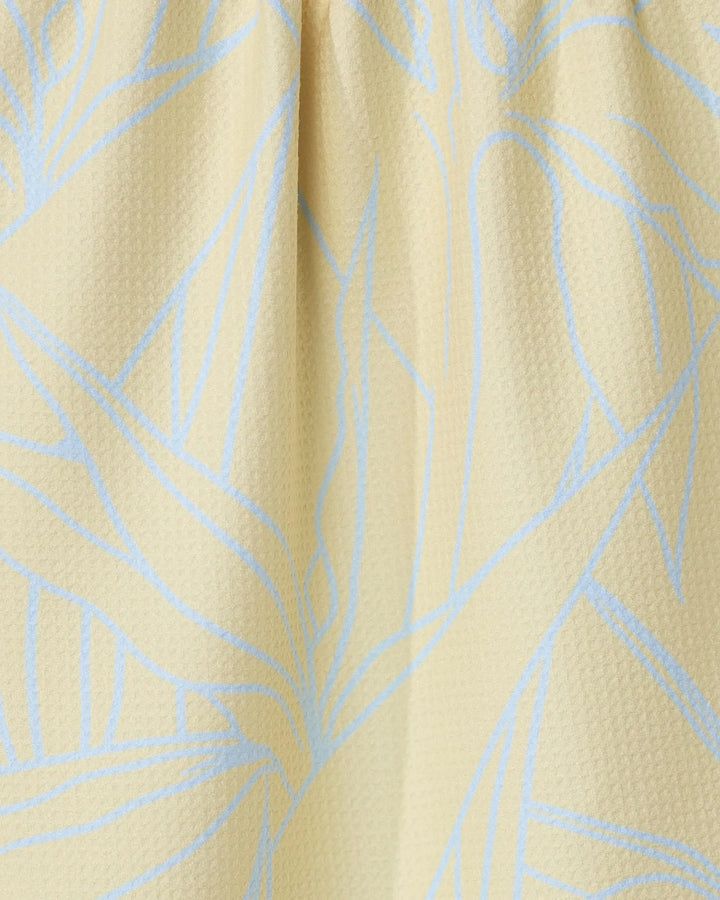Close-up of the Paradise Blooms tea towel by GEOMETRY, featuring a textured light yellow fabric with a subtle blue abstract leaf pattern and soft folds near the top.