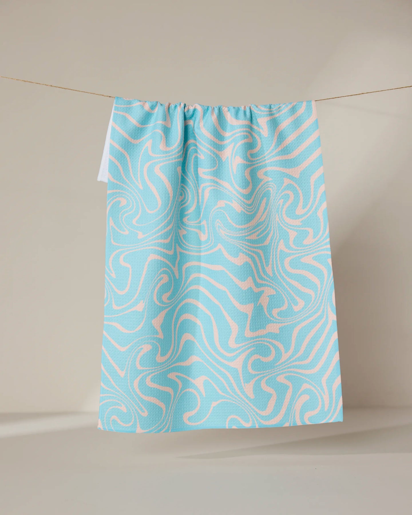 The GEOMETRY Patience tea towel, featuring a blue and white abstract swirl design, hangs against a neutral backdrop. Made from recycled materials, it’s both eco-friendly and quick-drying.