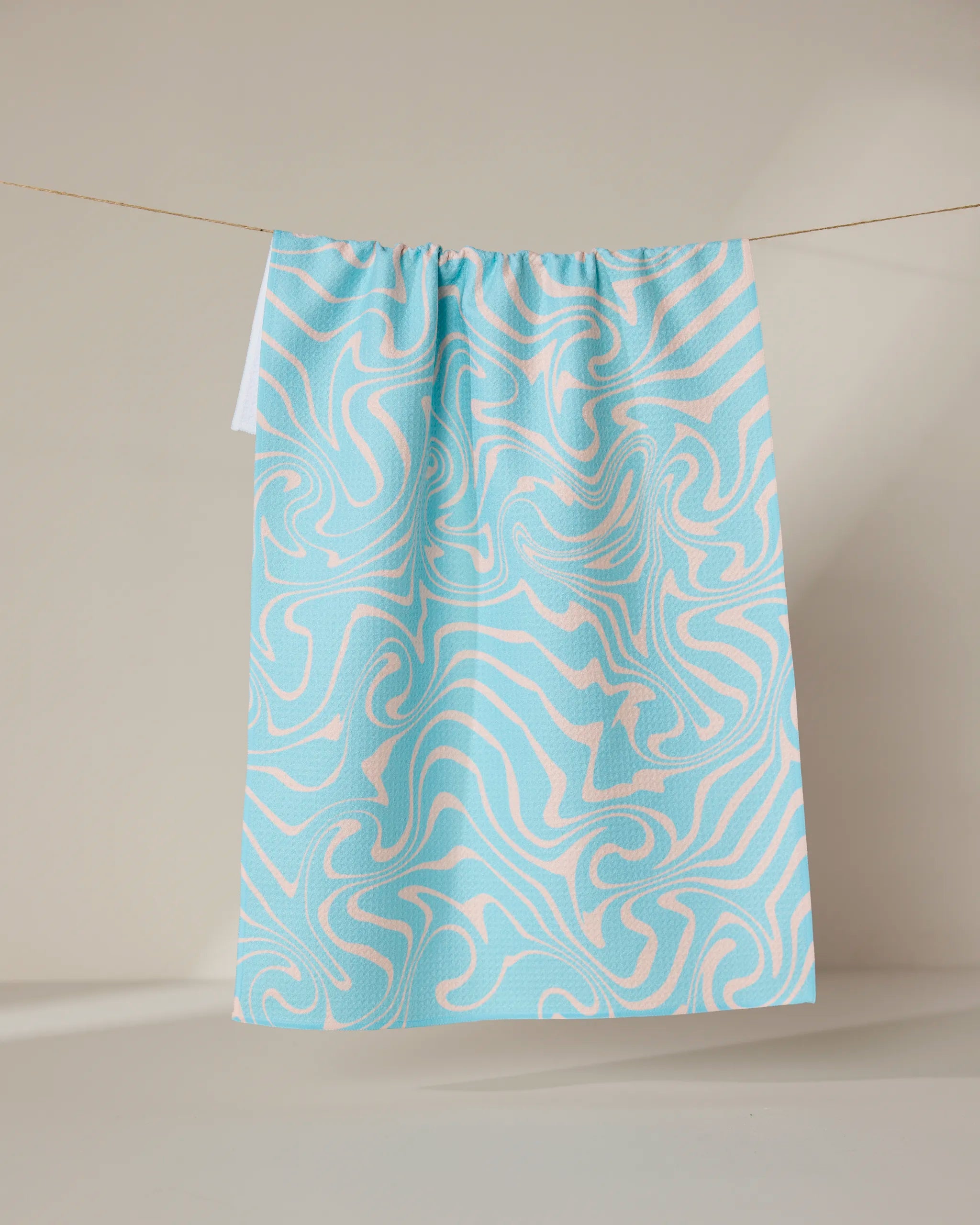 The GEOMETRY Patience tea towel, featuring a blue and white abstract swirl design, hangs against a neutral backdrop. Made from recycled materials, it’s both eco-friendly and quick-drying.