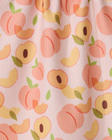 The GEOMETRY Peaches kitchen tea towel features whole peaches, halves, and slices with green leaves on a light pink background. Made from recycled materials with slightly visible fabric texture.