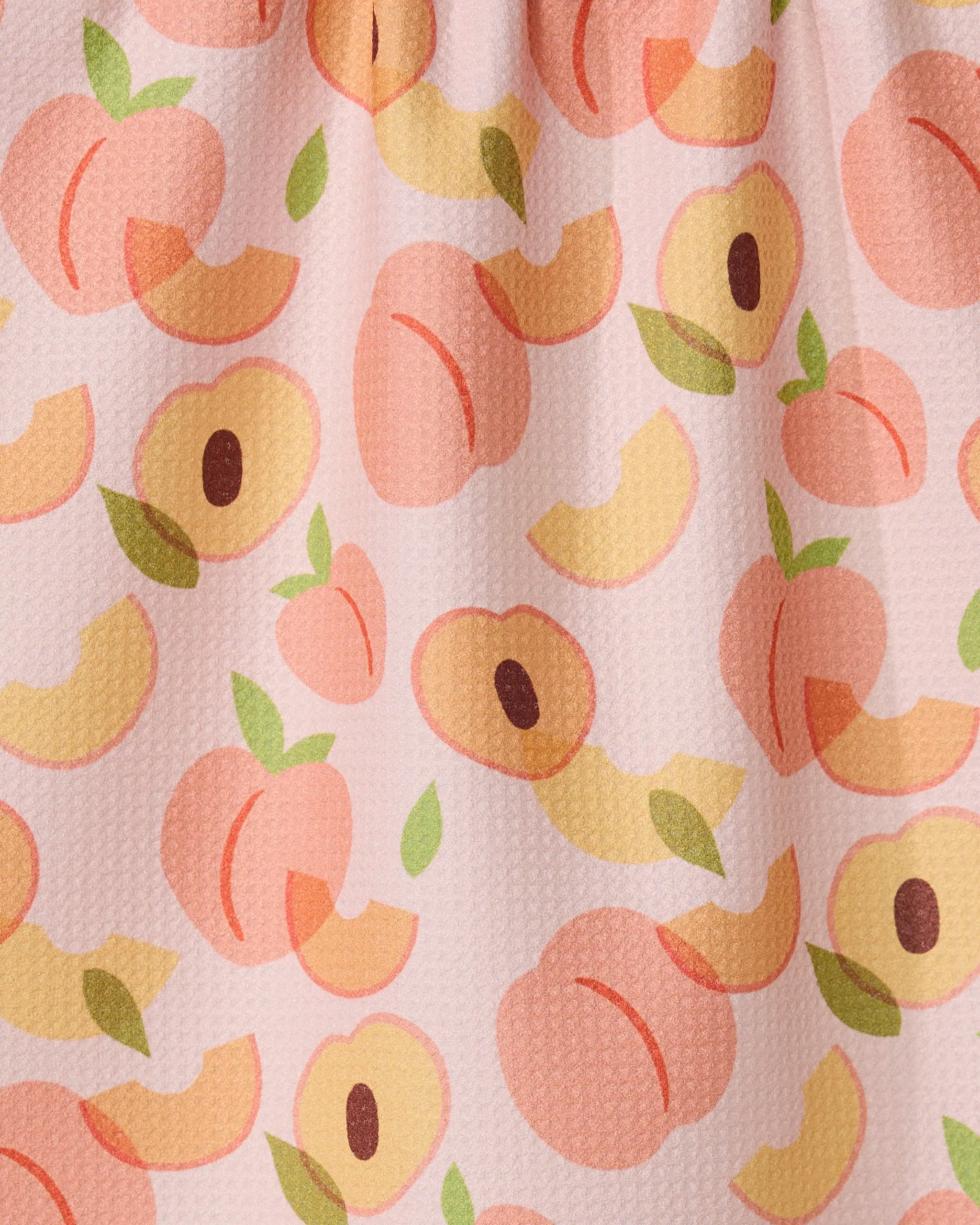 The GEOMETRY Peaches kitchen tea towel features whole peaches, halves, and slices with green leaves on a light pink background. Made from recycled materials with slightly visible fabric texture.