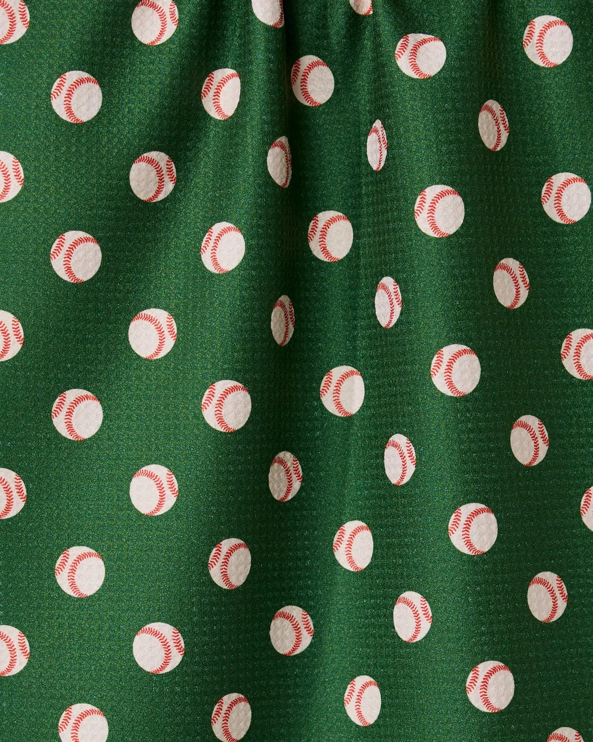 The Play Ball kitchen towel by GEOMETRY features green fabric adorned with white baseballs and red stitching, is slightly gathered at the top, and crafted from recycled materials.