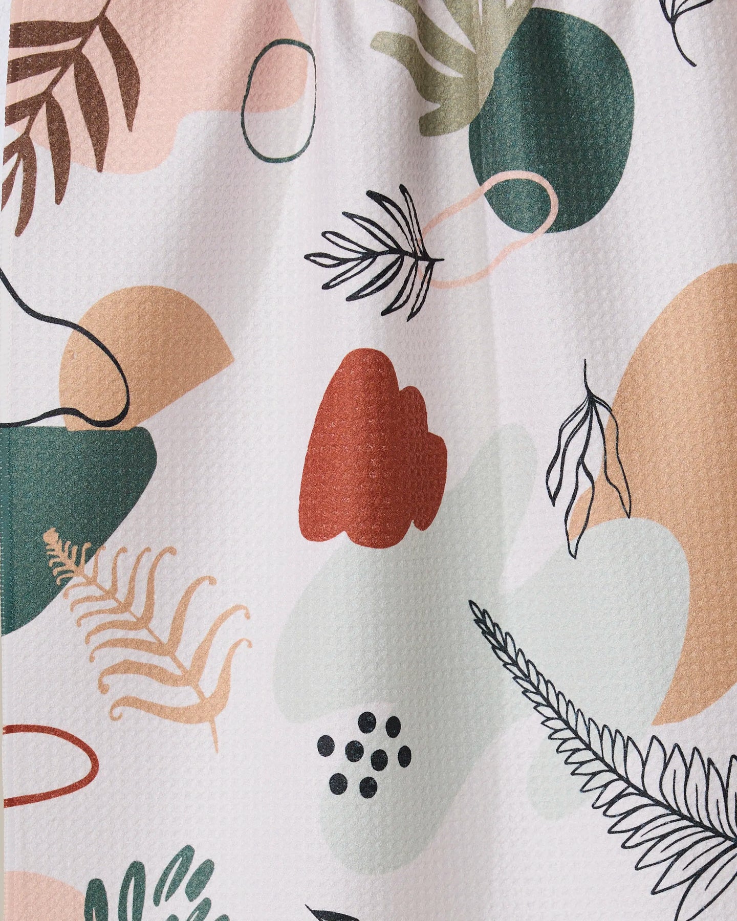 Plated Ferns by GEOMETRY features an abstract pattern of organic shapes and botanical elements in green, peach, black, and red on a light background. This playful, modern tea towel is made from recycled materials.