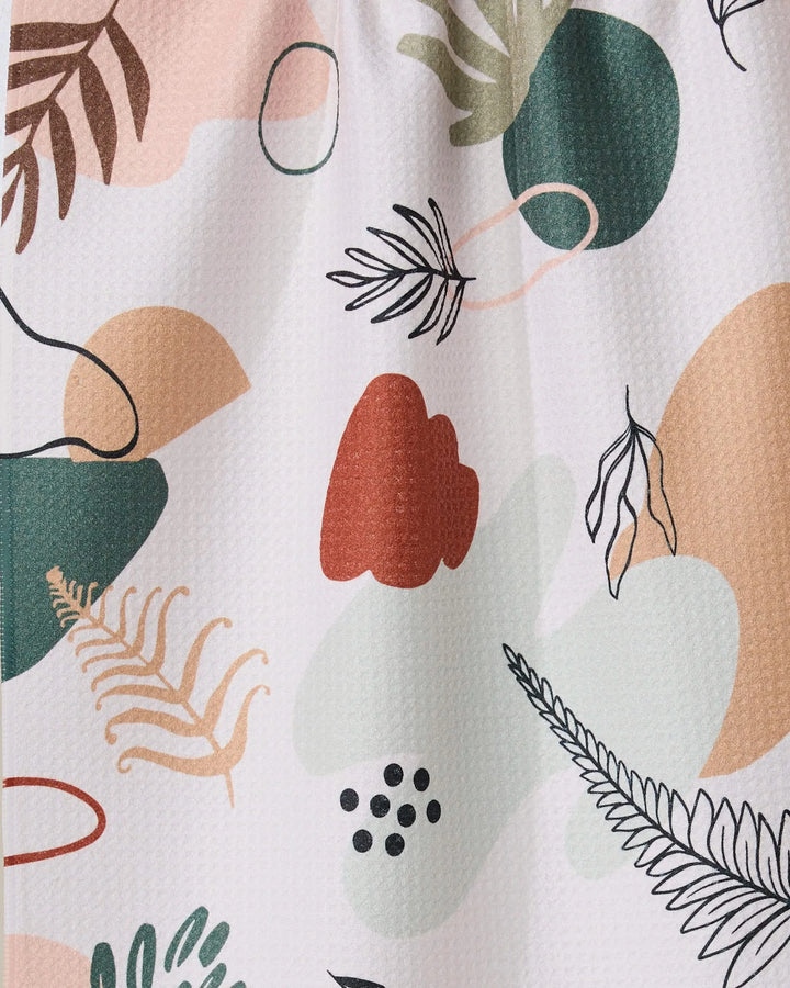 Plated Ferns by GEOMETRY features an abstract pattern of organic shapes and botanical elements in green, peach, black, and red on a light background. This playful, modern tea towel is made from recycled materials.