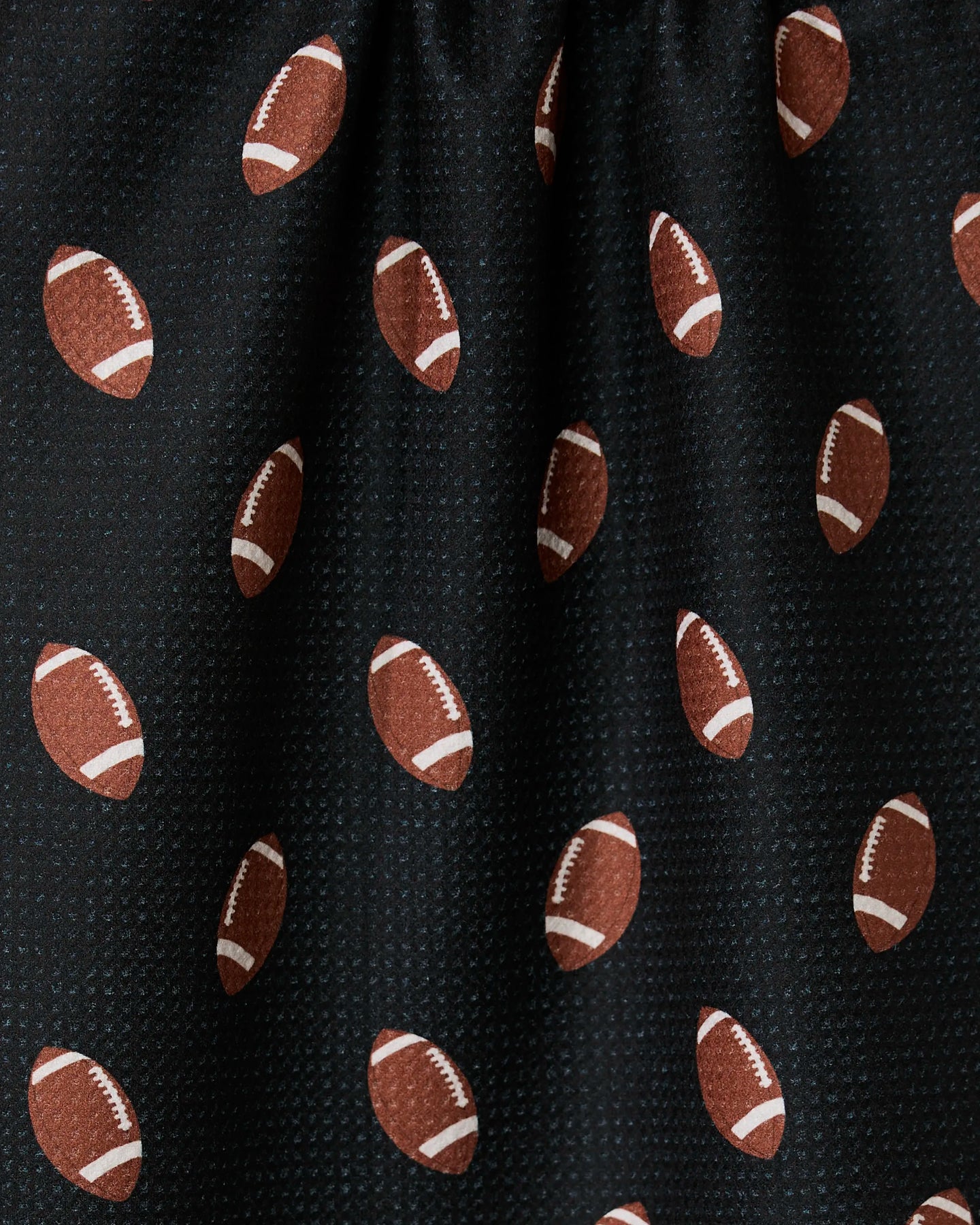 A close-up of GEOMETRYs Quarter Back ultra-absorbent black fabric, featuring a repeating pattern of brown footballs with white laces and stripes—slightly gathered at the top and perfect for a sporty tea towel.