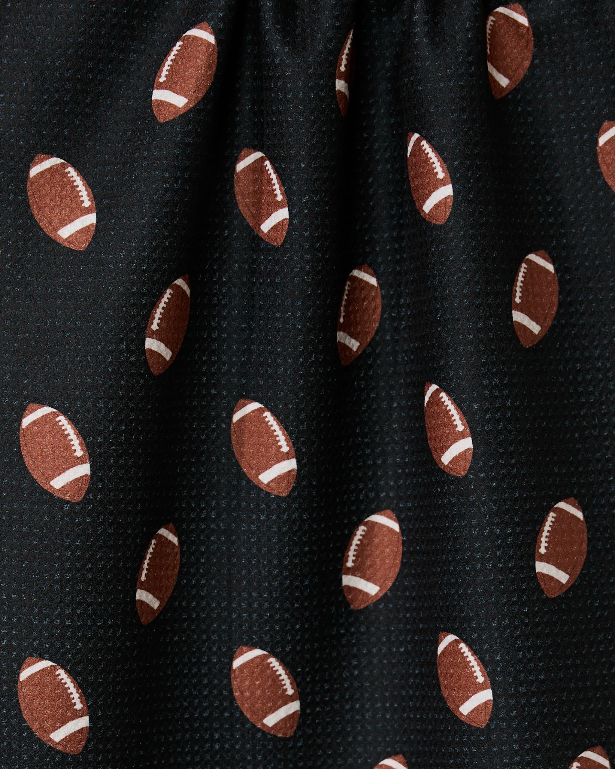 A close-up of GEOMETRYs Quarter Back ultra-absorbent black fabric, featuring a repeating pattern of brown footballs with white laces and stripes—slightly gathered at the top and perfect for a sporty tea towel.
