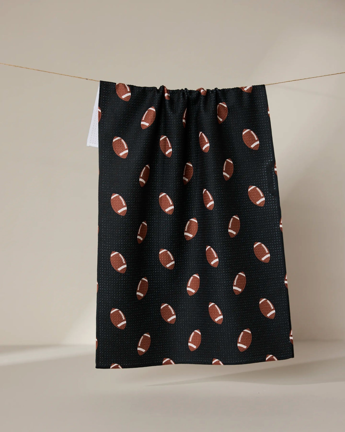 The GEOMETRY Quarter Back is a black tea towel made from recycled materials, decorated with brown and white football patterns, and shown hanging against a neutral background.