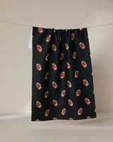 The GEOMETRY Quarter Back is a black tea towel made from recycled materials, decorated with brown and white football patterns, and shown hanging against a neutral background.