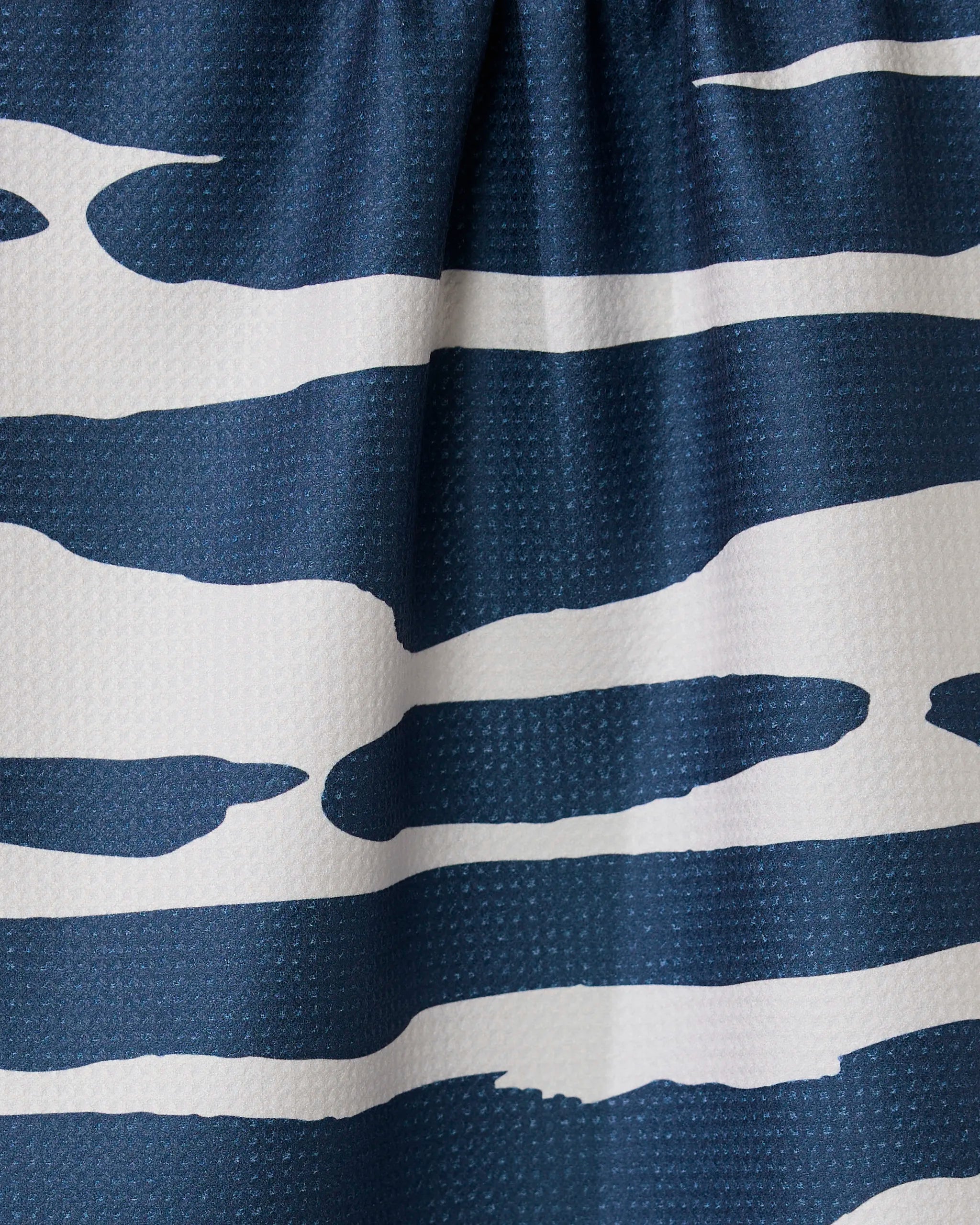 Close-up of the GEOMETRY Reflected - Midnight tea towel, made from recycled materials, with ultra-absorbency and a blue and white abstract wave-like striped pattern gathered at the top.