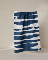 The GEOMETRY Reflected - Midnight tea towel, crafted from ultra-absorbent recycled materials, features bold, irregular navy blue stripes on white and hangs on a thin clothesline against a neutral backdrop.