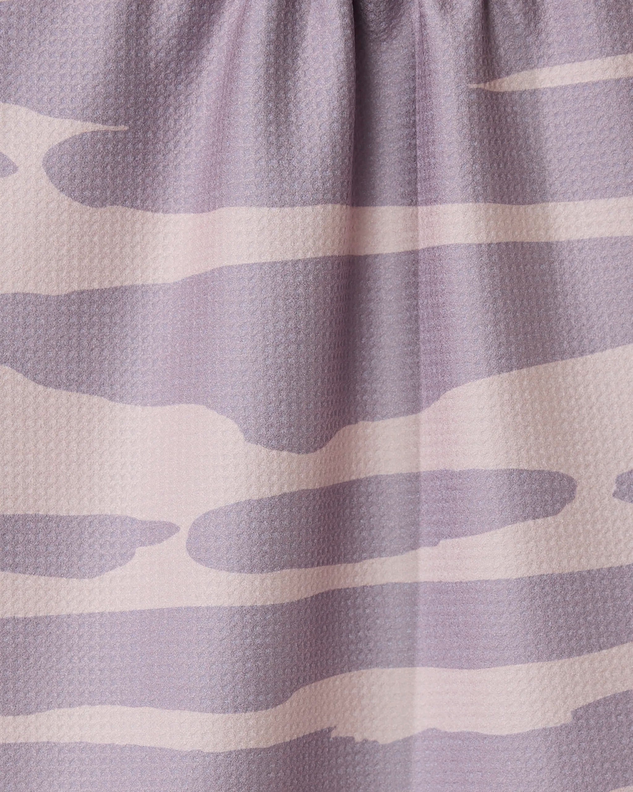 Close-up of the GEOMETRY Reflected - Sunset tea towel, made from recycled materials and featuring a light purple and beige abstract wavy pattern. The fabric is slightly gathered at the top.