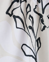 Reflected by GEOMETRY features a black line drawing of a stylized plant with leaves and stems on a textured white tea towel, crafted from recycled materials with subtle light beige patterns.