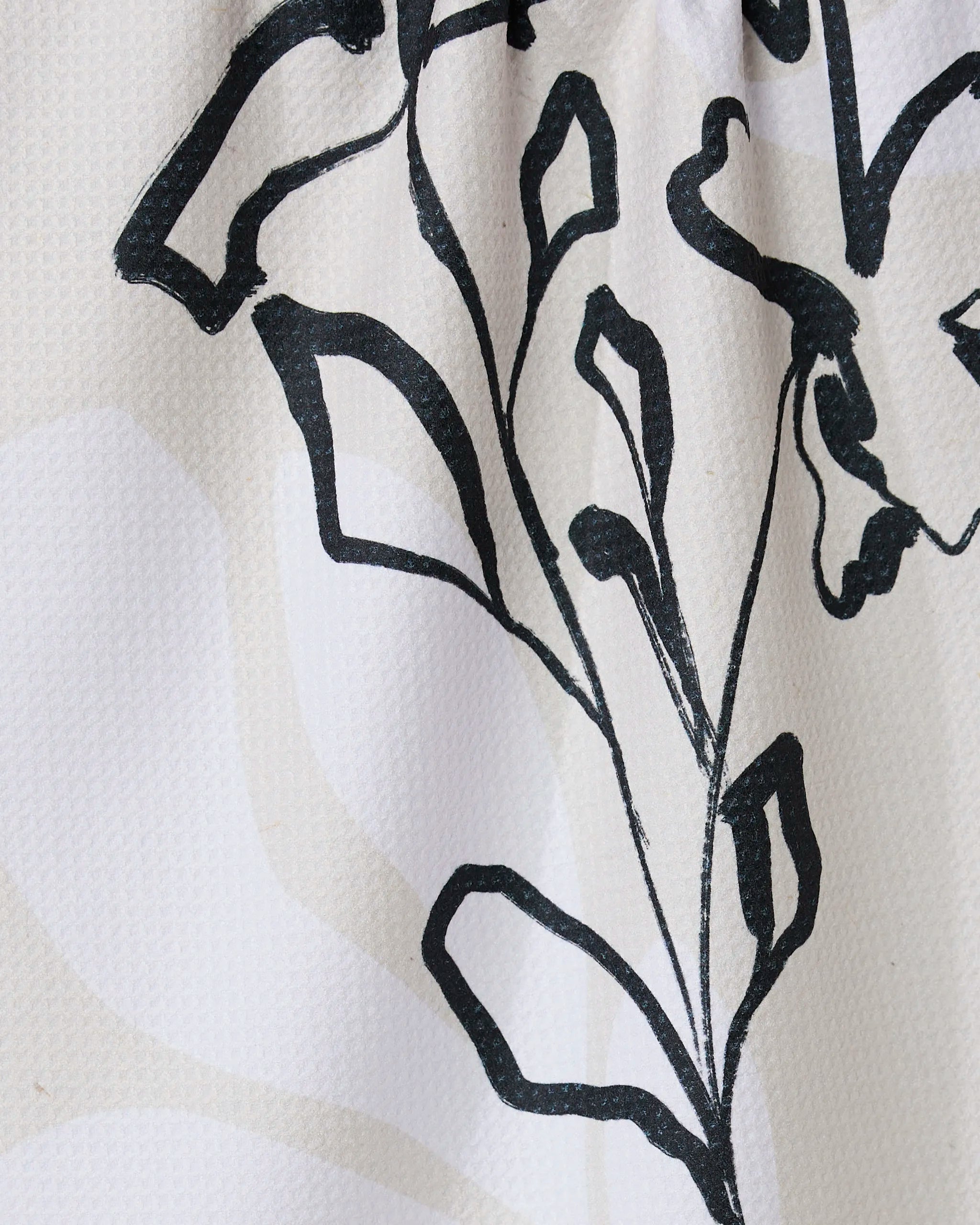 Reflected by GEOMETRY features a black line drawing of a stylized plant with leaves and stems on a textured white tea towel, crafted from recycled materials with subtle light beige patterns.