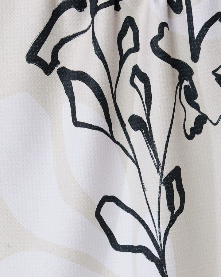 Reflected by GEOMETRY features a black line drawing of a stylized plant with leaves and stems on a textured white tea towel, crafted from recycled materials with subtle light beige patterns.