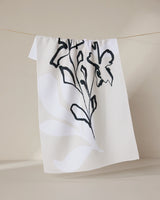 The GEOMETRY Reflected tea towel, made from recycled materials, features a minimalist black and gray botanical design and is shown hanging on a thin string against a neutral background.