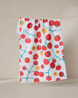 The GEOMETRY Ripe recycled kitchen towel, featuring vibrant red and orange cherry tomatoes on green vines, hangs on a clothesline against a neutral background.