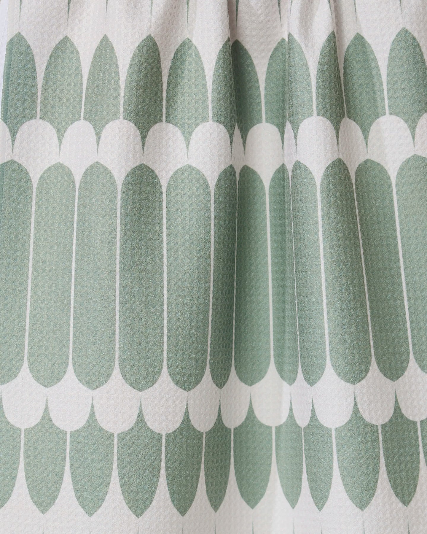 Close-up of GEOMETRY’s Salle Verte tea towel, showing its repeating green oval geometric pattern and white scalloped edges. The ultra-absorbent, textured towel features a modern symmetrical design with visible folds for added depth.