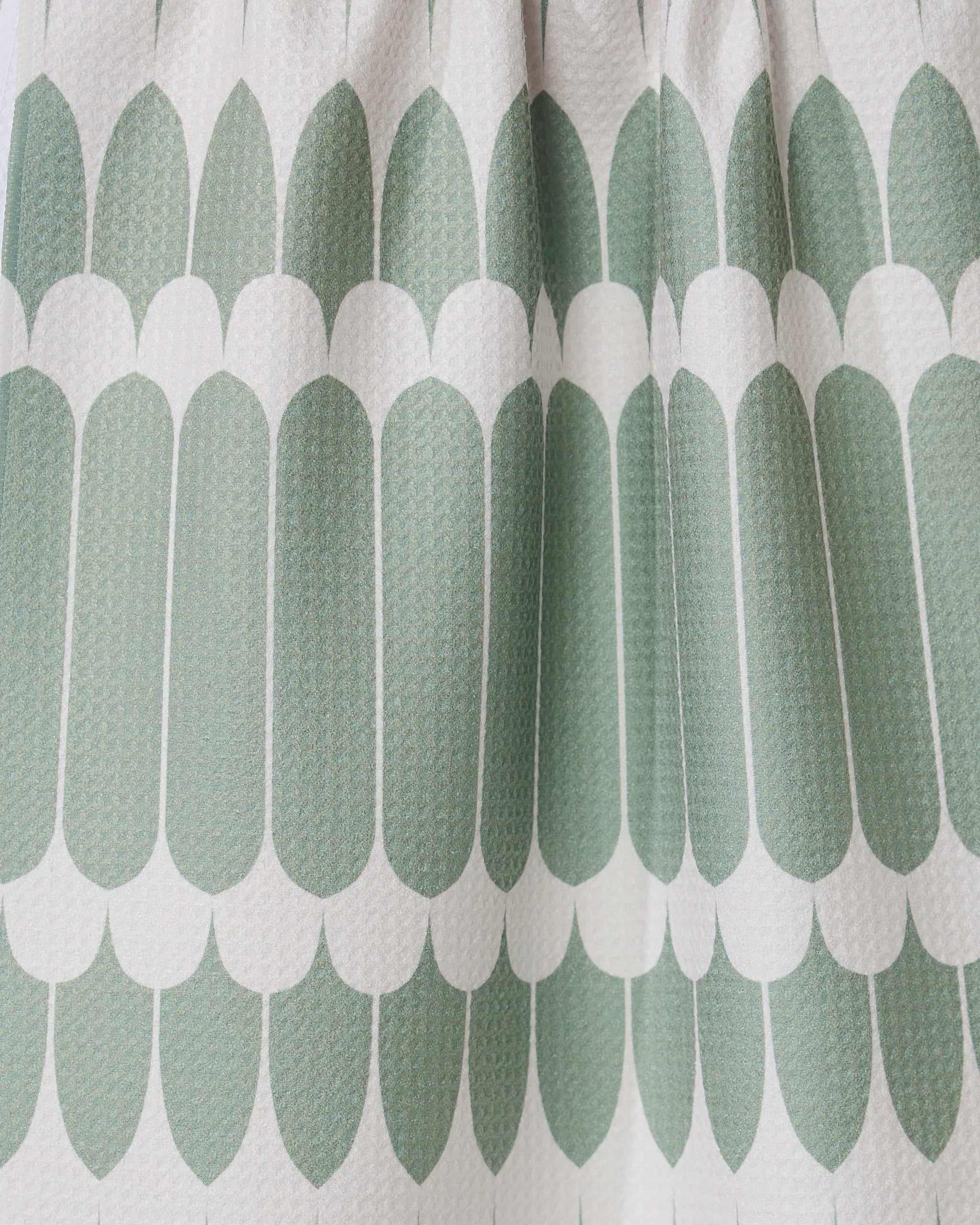 Close-up of GEOMETRY’s Salle Verte tea towel, showing its repeating green oval geometric pattern and white scalloped edges. The ultra-absorbent, textured towel features a modern symmetrical design with visible folds for added depth.