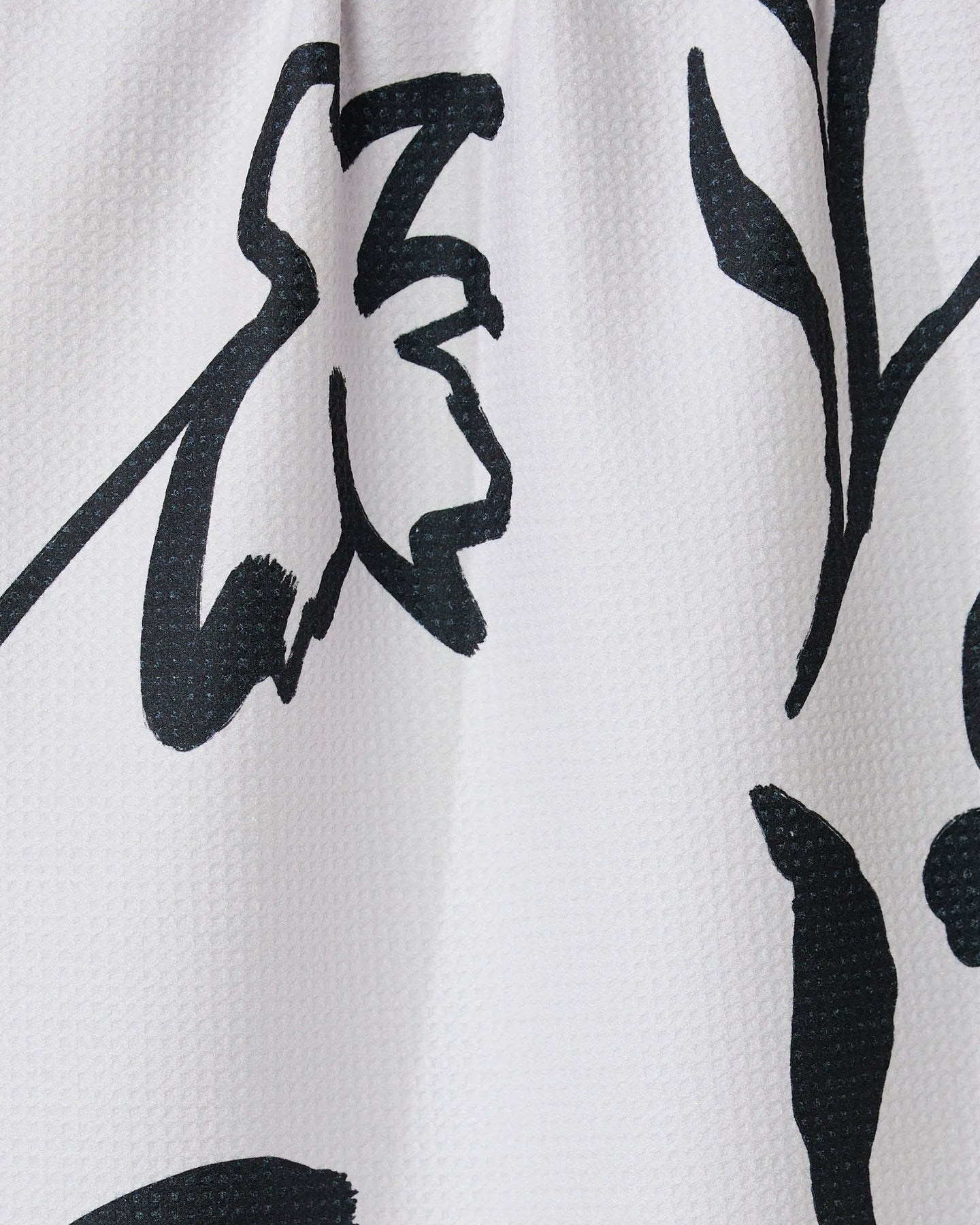 Close-up of the Shade tea towel by GEOMETRY, crafted from recycled materials. It features a bold black abstract floral print with thick, sweeping lines forming flower and leaf shapes on a white textured background.