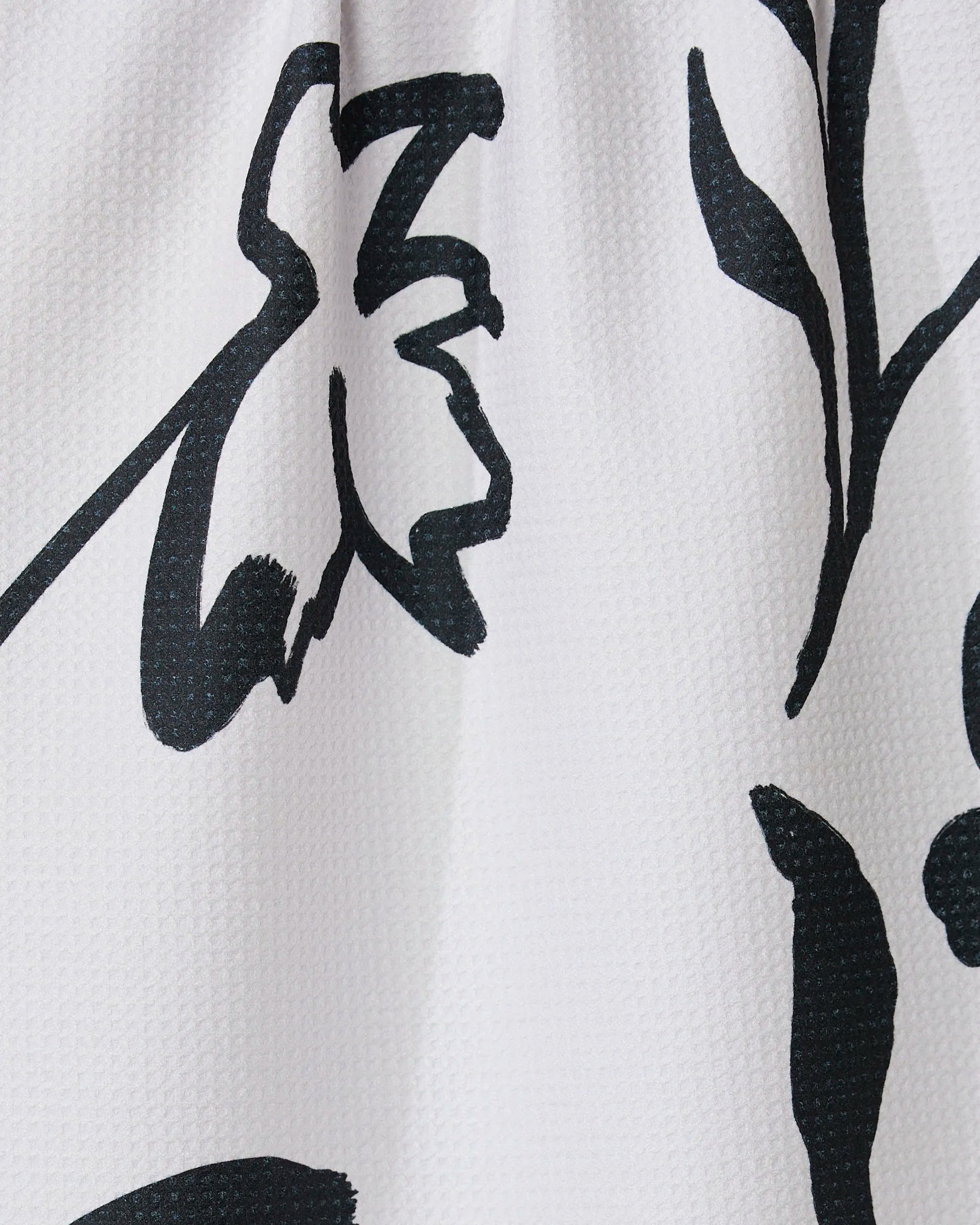 Close-up of the Shade tea towel by GEOMETRY, crafted from recycled materials. It features a bold black abstract floral print with thick, sweeping lines forming flower and leaf shapes on a white textured background.