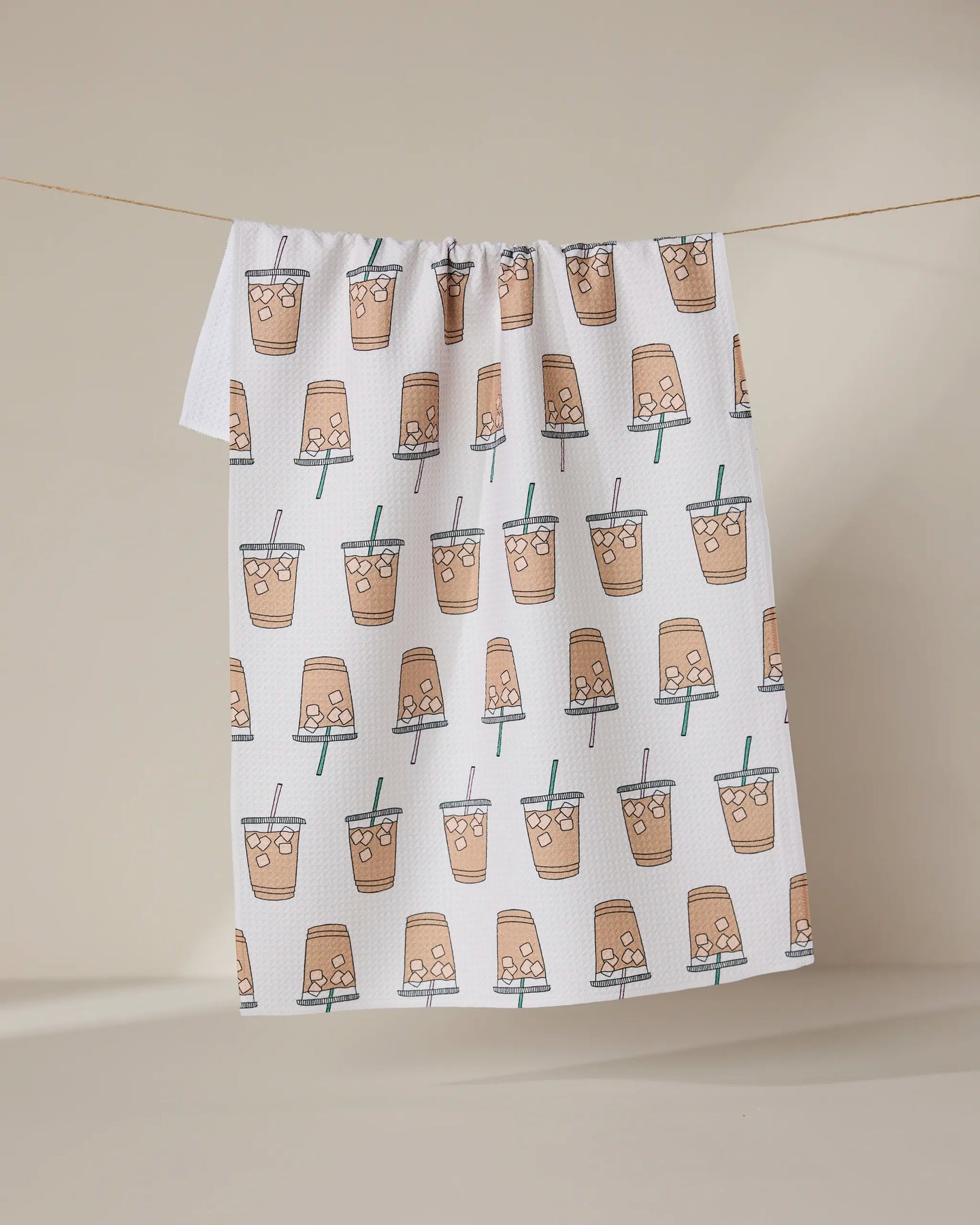 The GEOMETRY Sippin on Summer towel, ultra-absorbent and white with a repeating illustrated bubble tea cup pattern, hangs on a clothesline against a neutral background.