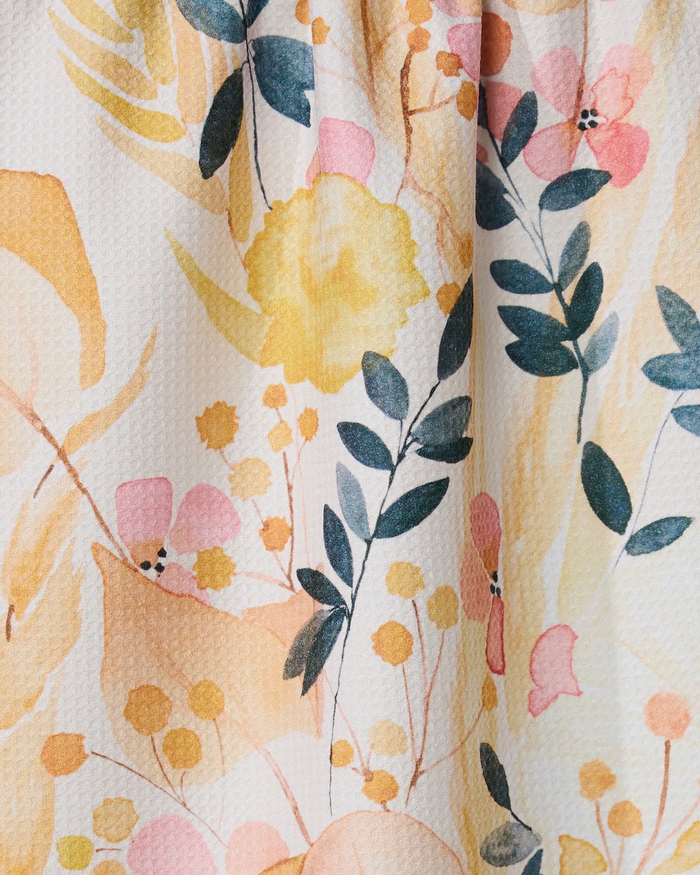 The GEOMETRY Sleepy Fields kitchen towel features a watercolor floral print—yellow, pink, and orange blooms with green leaves—on textured white fabric made from recycled materials.