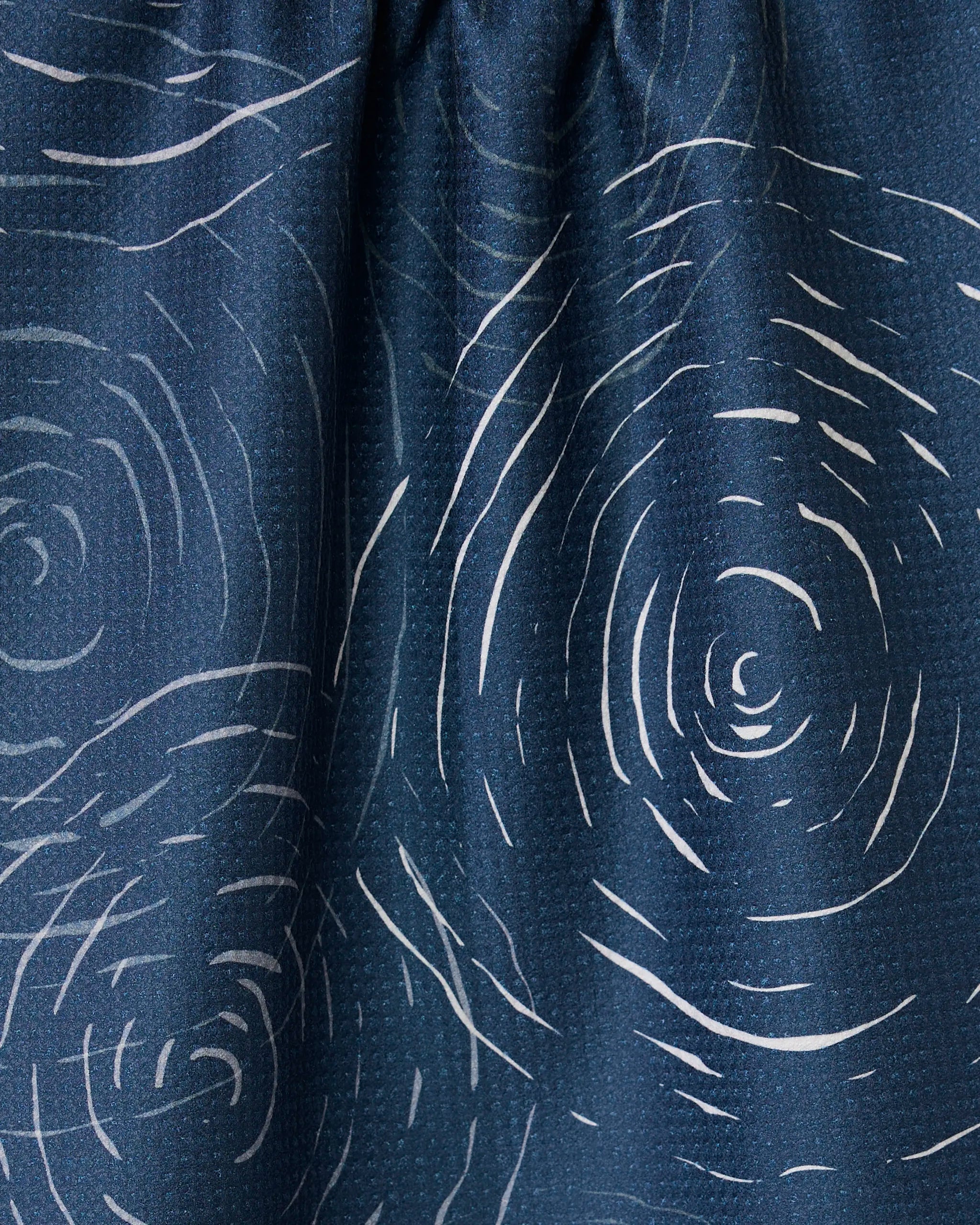 Close-up of GEOMETRYs Soft Steps - Midnight, a dark blue kitchen towel made from recycled materials. Features white, ripple-like lines in an abstract wave pattern with slight gathers at the top.