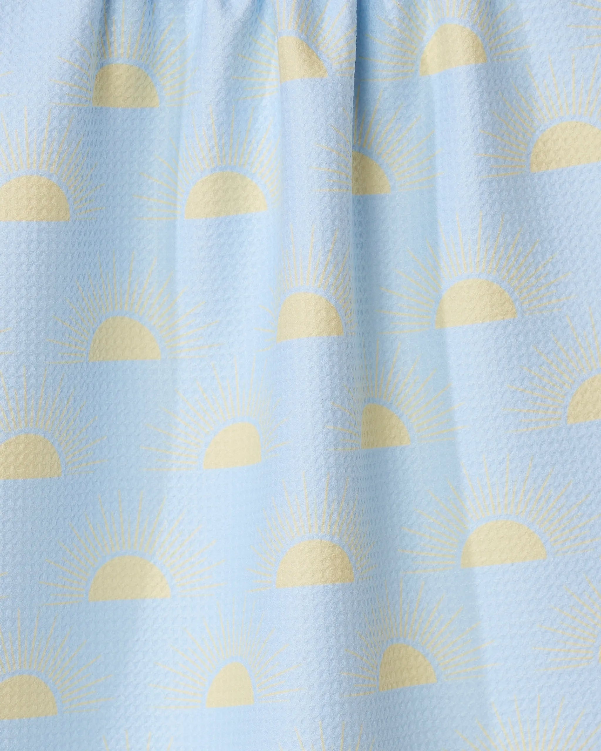 The GEOMETRY Soft Summer Sun tea towel features a light blue textured design with yellow half sun and sunbeam patterns, made from recycled materials.