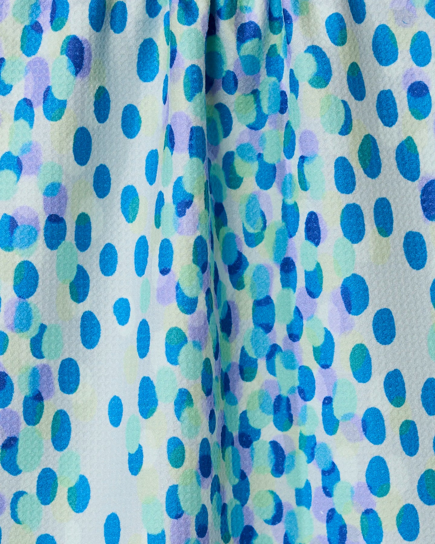 Spotty Summer by GEOMETRY: a close-up of recycled fabric with a textured, lightly gathered surface, showcasing irregular blue, teal, and lavender dots on a light background.